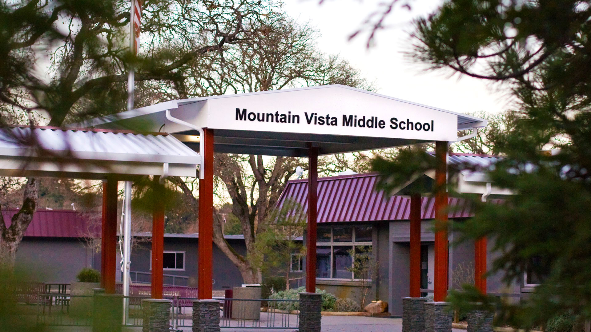 Metal shade structure, with red posts and white tops, with the school name lettered at the entrance.