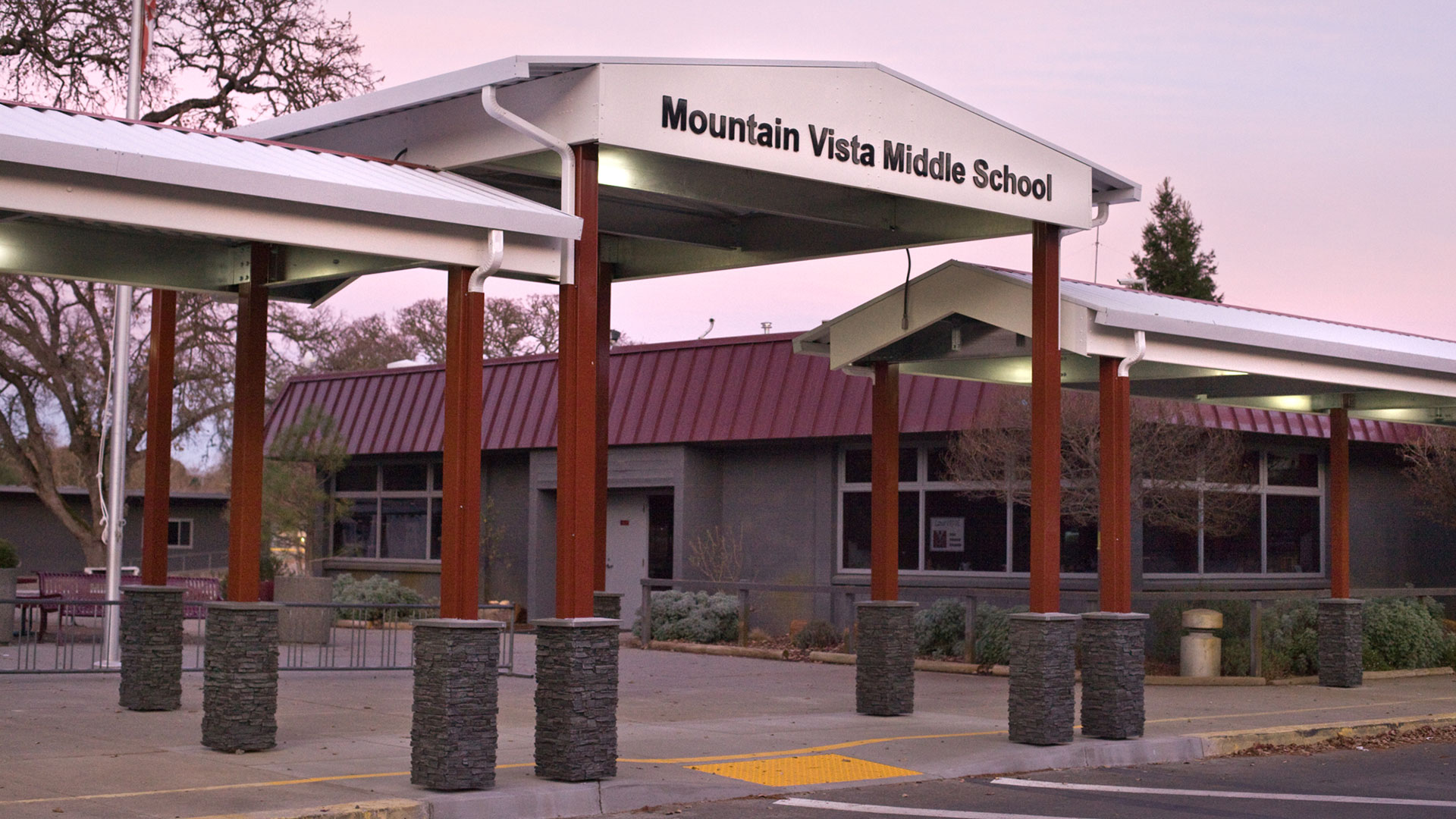 Metal shade structure, with red posts and white tops, with the school name lettered at the entrance.