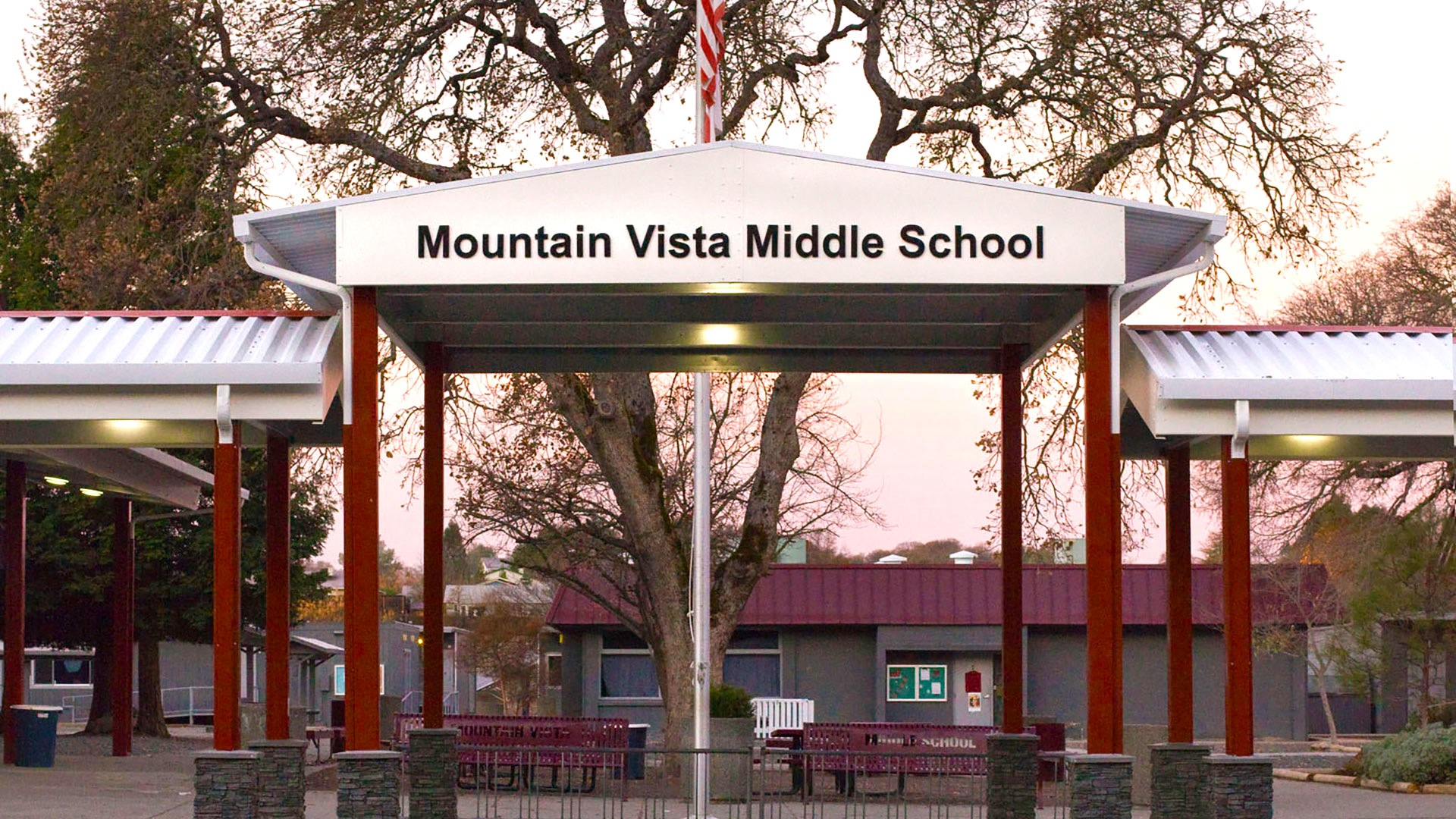 Metal shade structure, with red posts and white tops, with the school name lettered at the entrance.