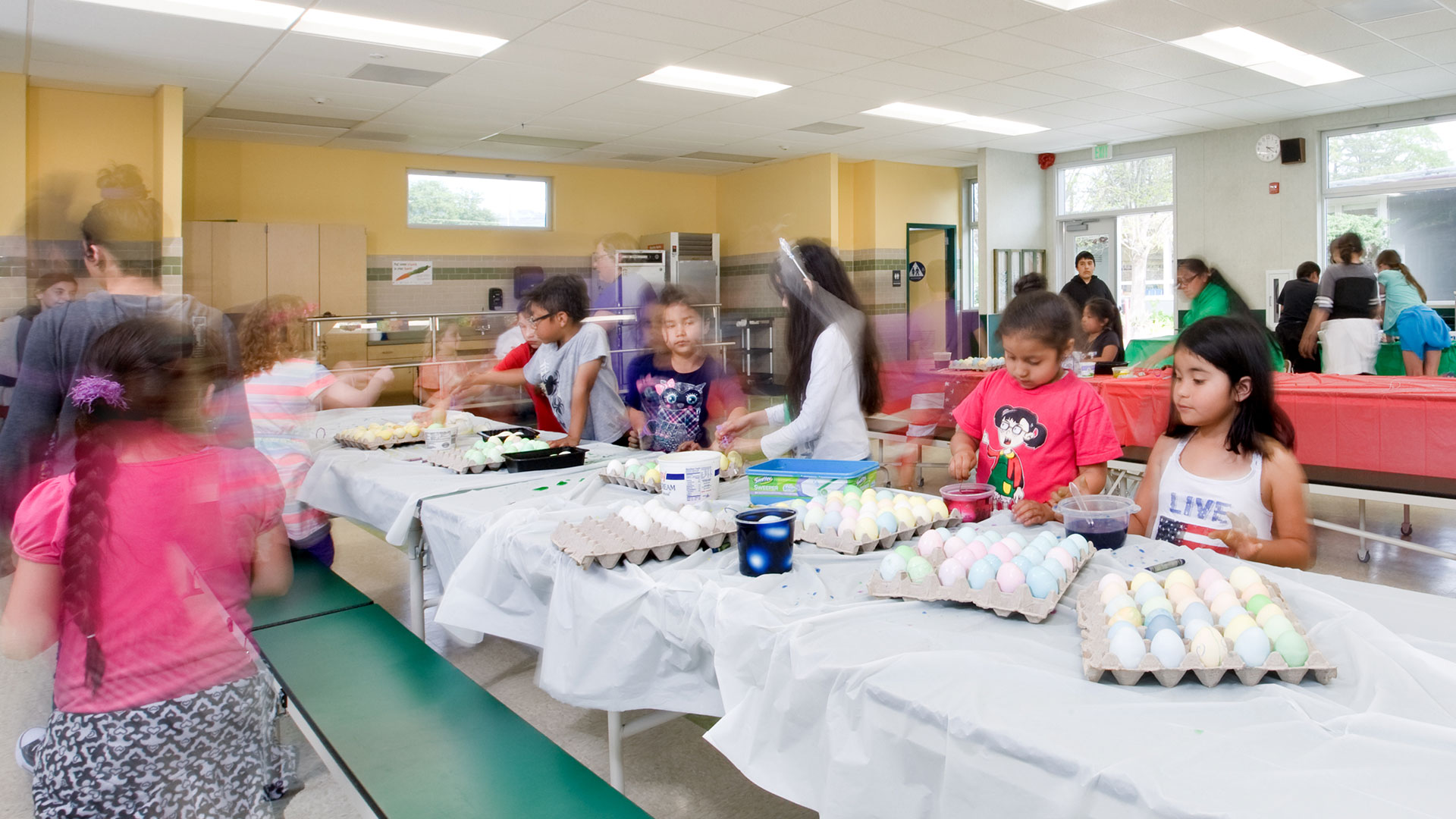 Interior of multi-use room, with students coloring eggs on covered tables.