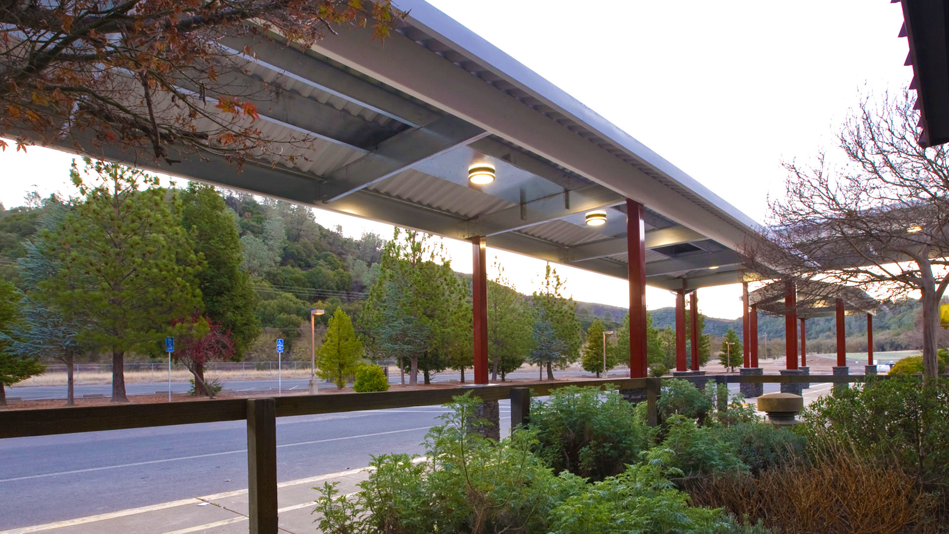 Canopies extending the walkway, with bushes in foreground and parking lot behind canopy.