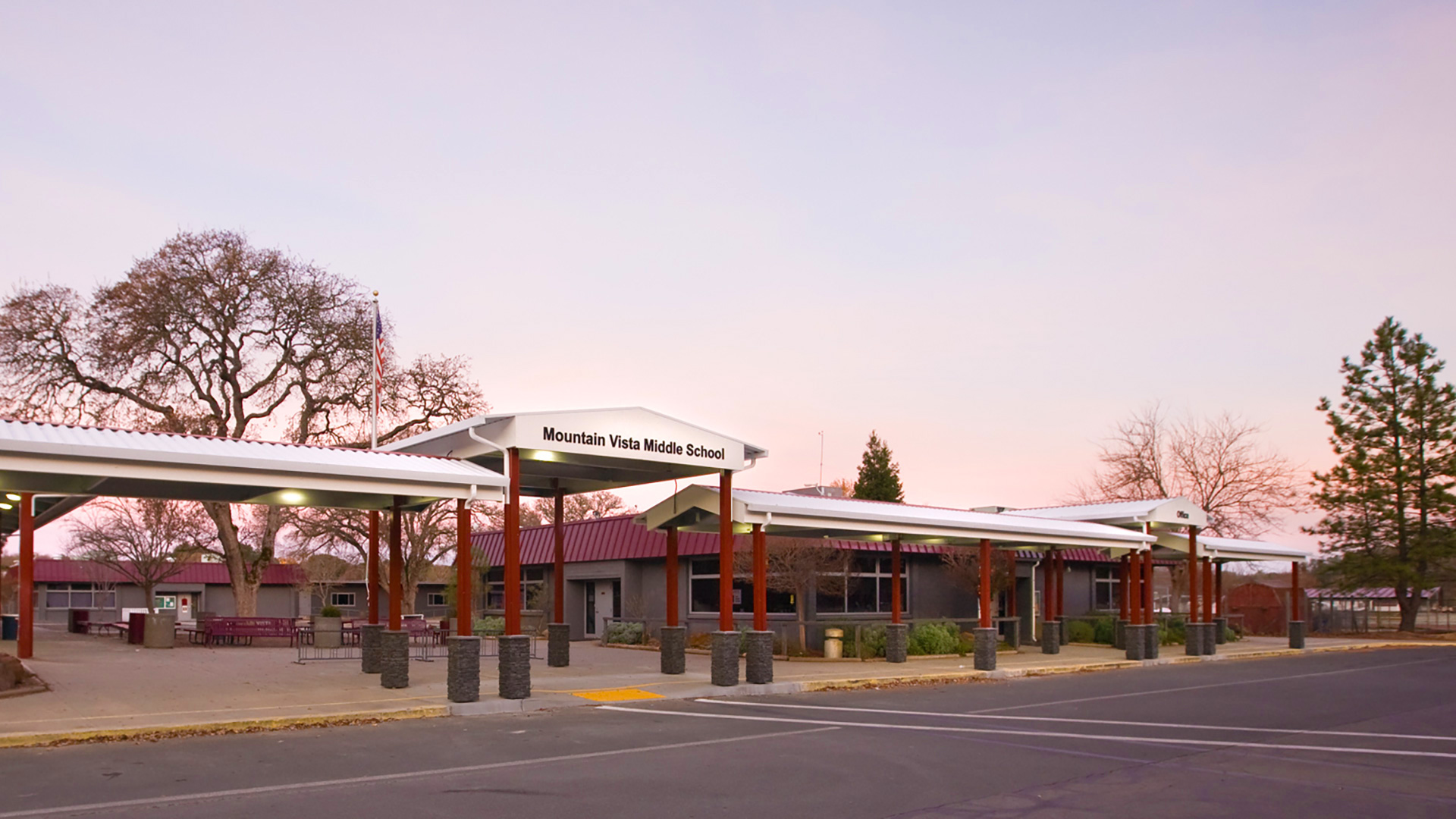 Metal shade structure, with red posts and white tops, with the school name lettered at the entrance.