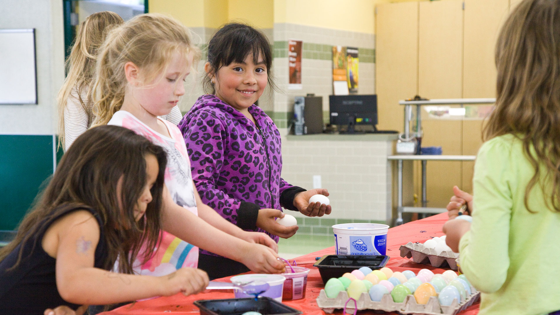 Interior of multi-use room, with students coloring eggs on covered tables.