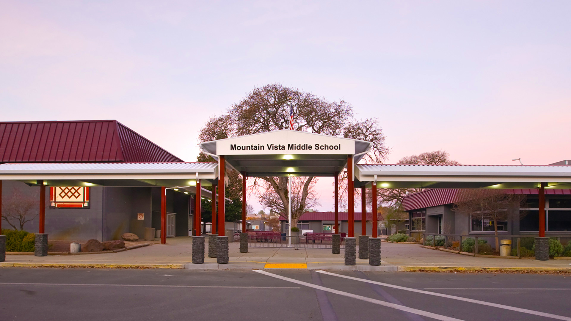 Metal shade structure, with red posts and white tops, with the school name lettered at the entrance.