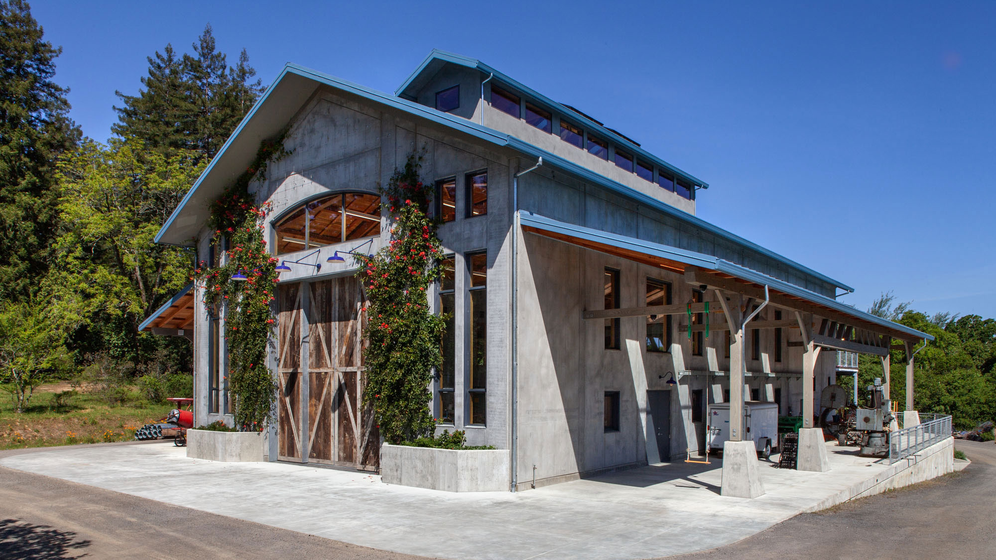 Double height concrete barn building, with tall windows, blue roof, and monitor