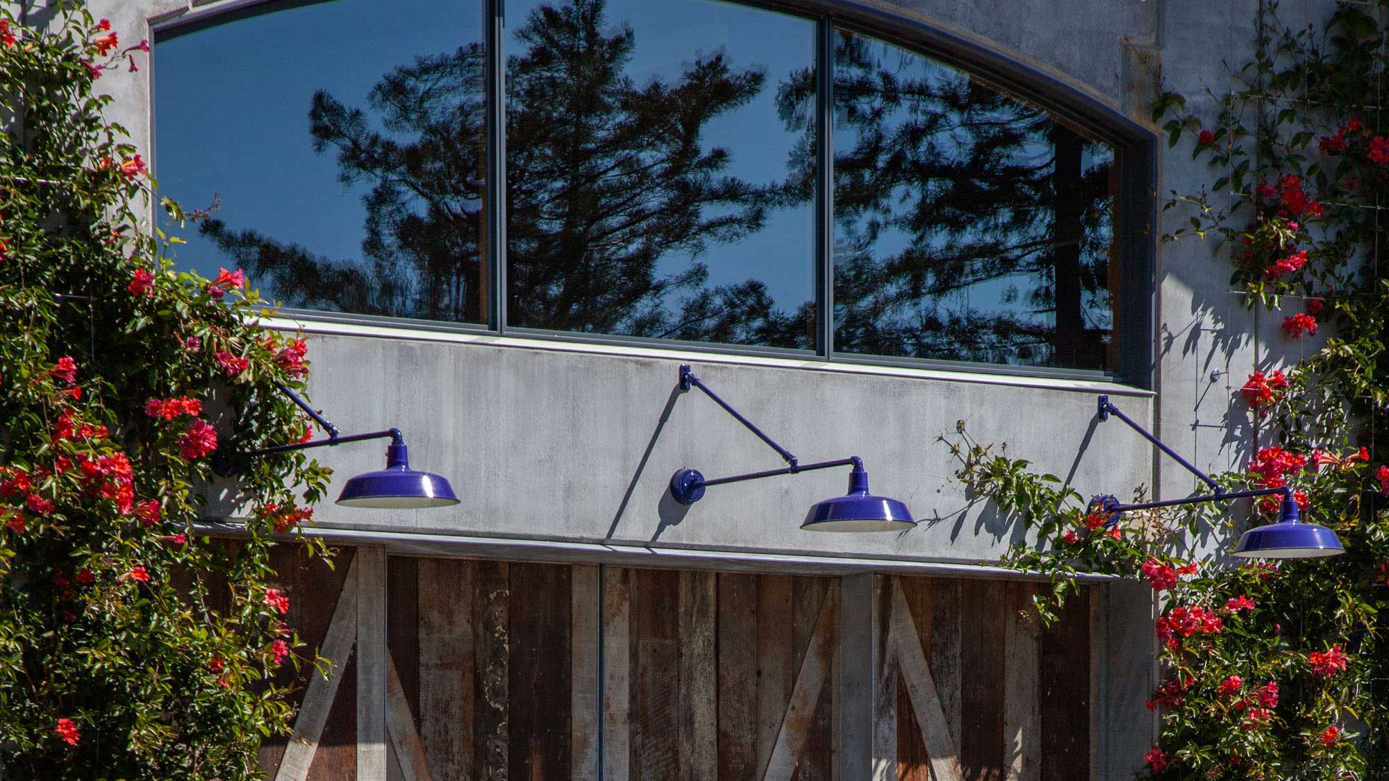 Close-up of 3 purple light fixtures over entrance to barn, wooden door beneath and large window above.