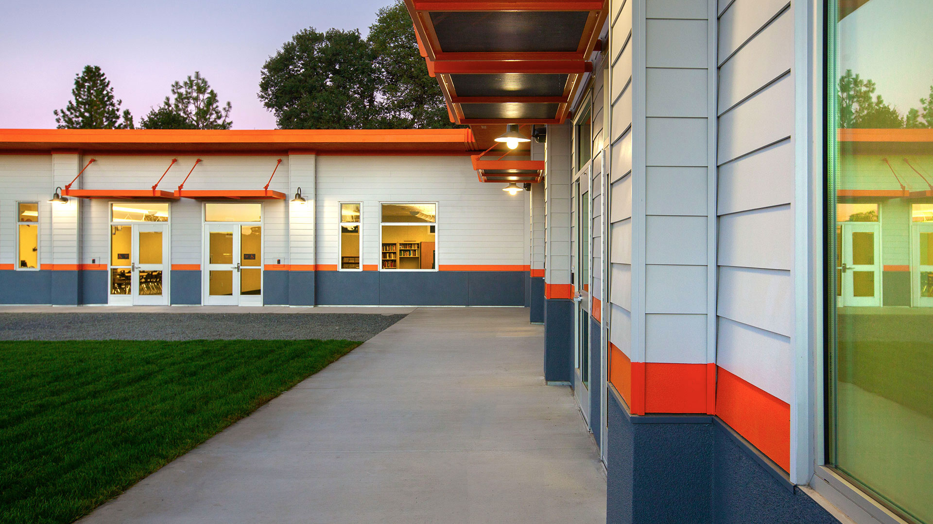 Classroom wing walkway, wide concrete walkway between wall and green, manicured grass.