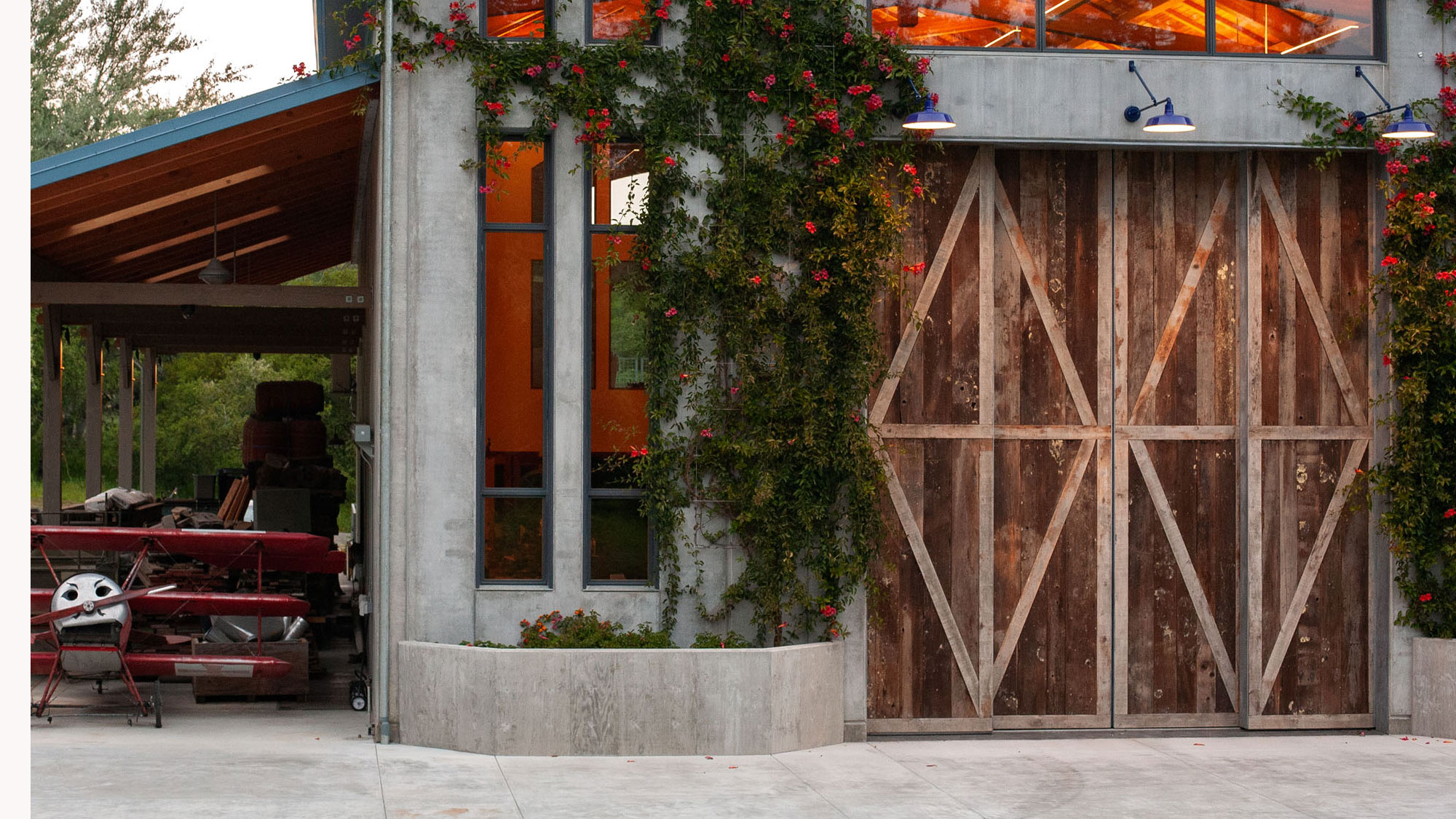 Concrete planters framing the main door exterior, with reaching green plants and tall windows behind.