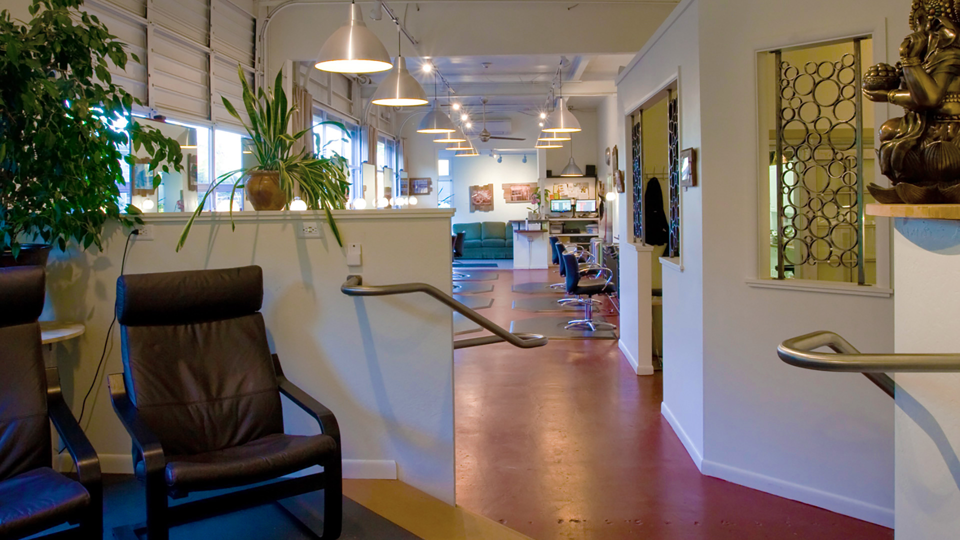 Interior of salon, salon chairs and mirrors stationed along red concrete floor, hanging pendent lights above.