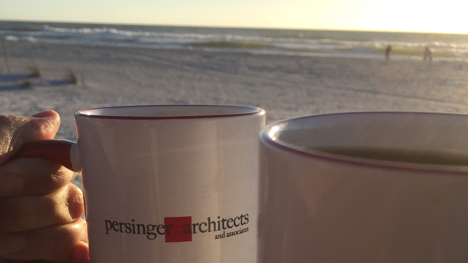Persinger mugs being clinked on a beach with ocean behind