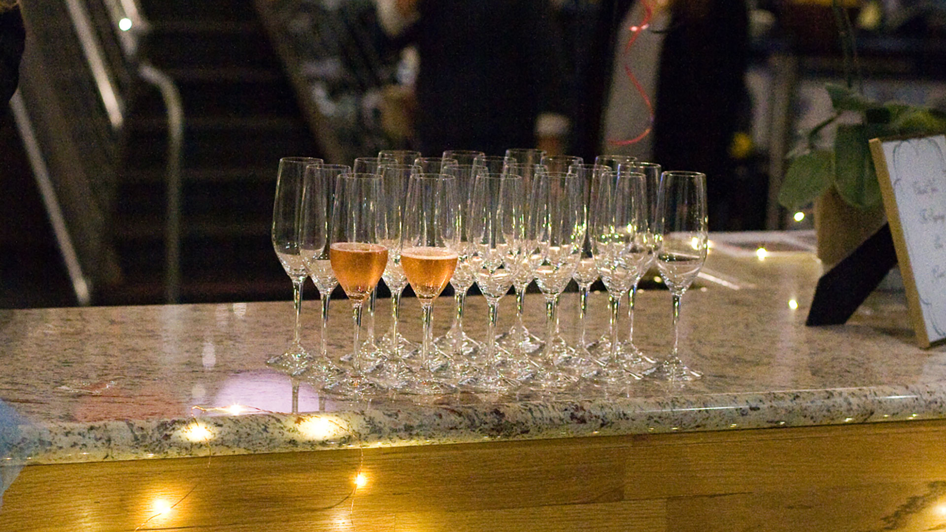 Group of champagne flutes on countertop, people gathering in background