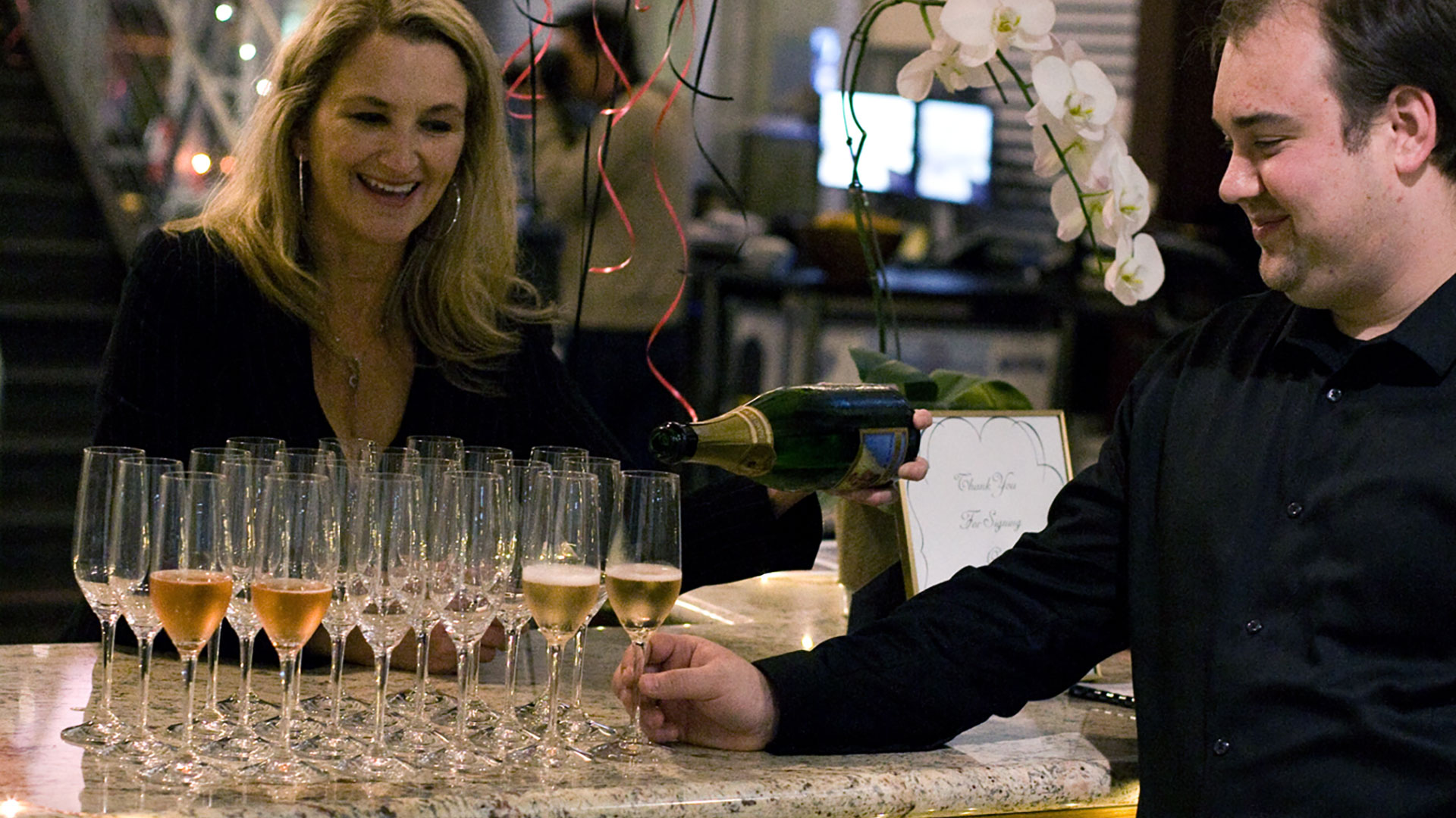 Man grabbing champagne flute from row of glasses, woman smiling behind