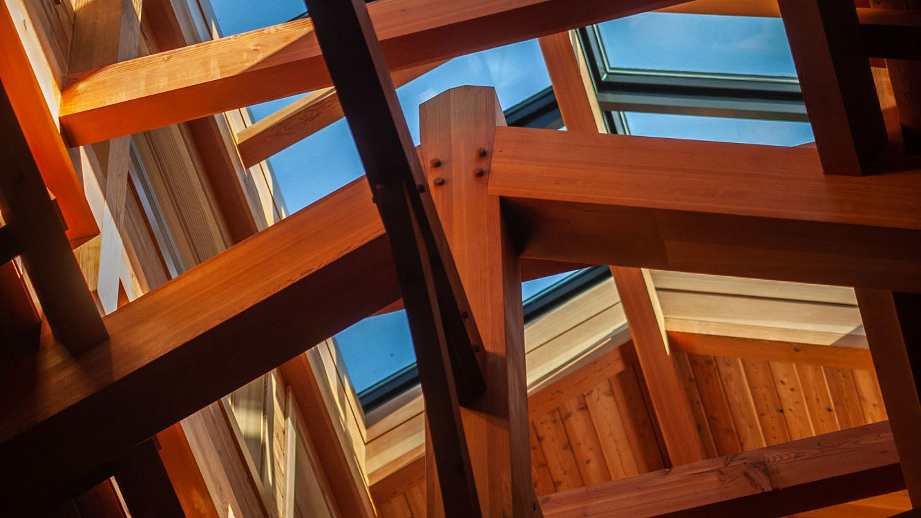 Closeup of wooden truss with blue skylight behind.