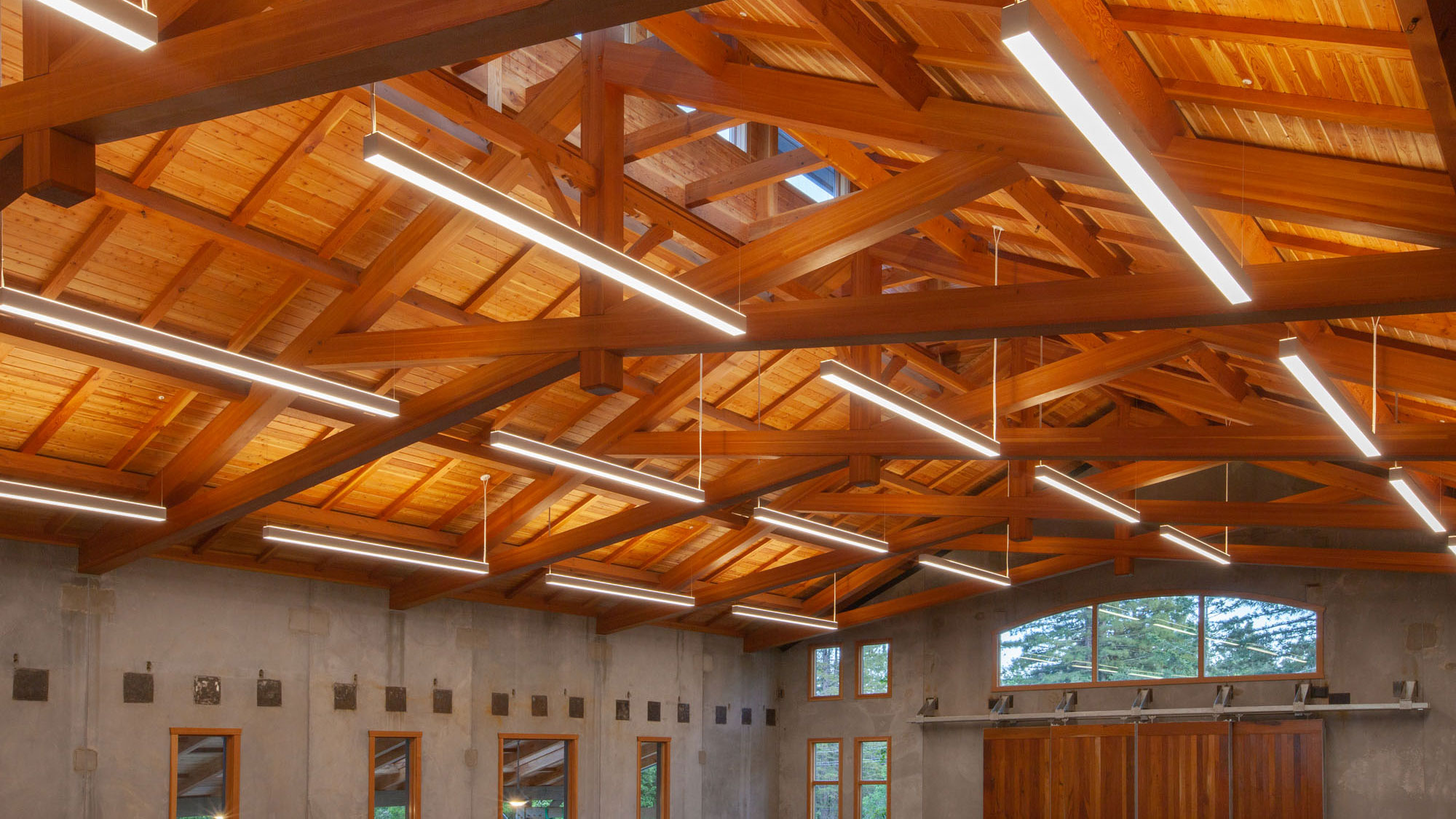 Expanse of brown wooden truss, juxtaposed against gray concrete walls.