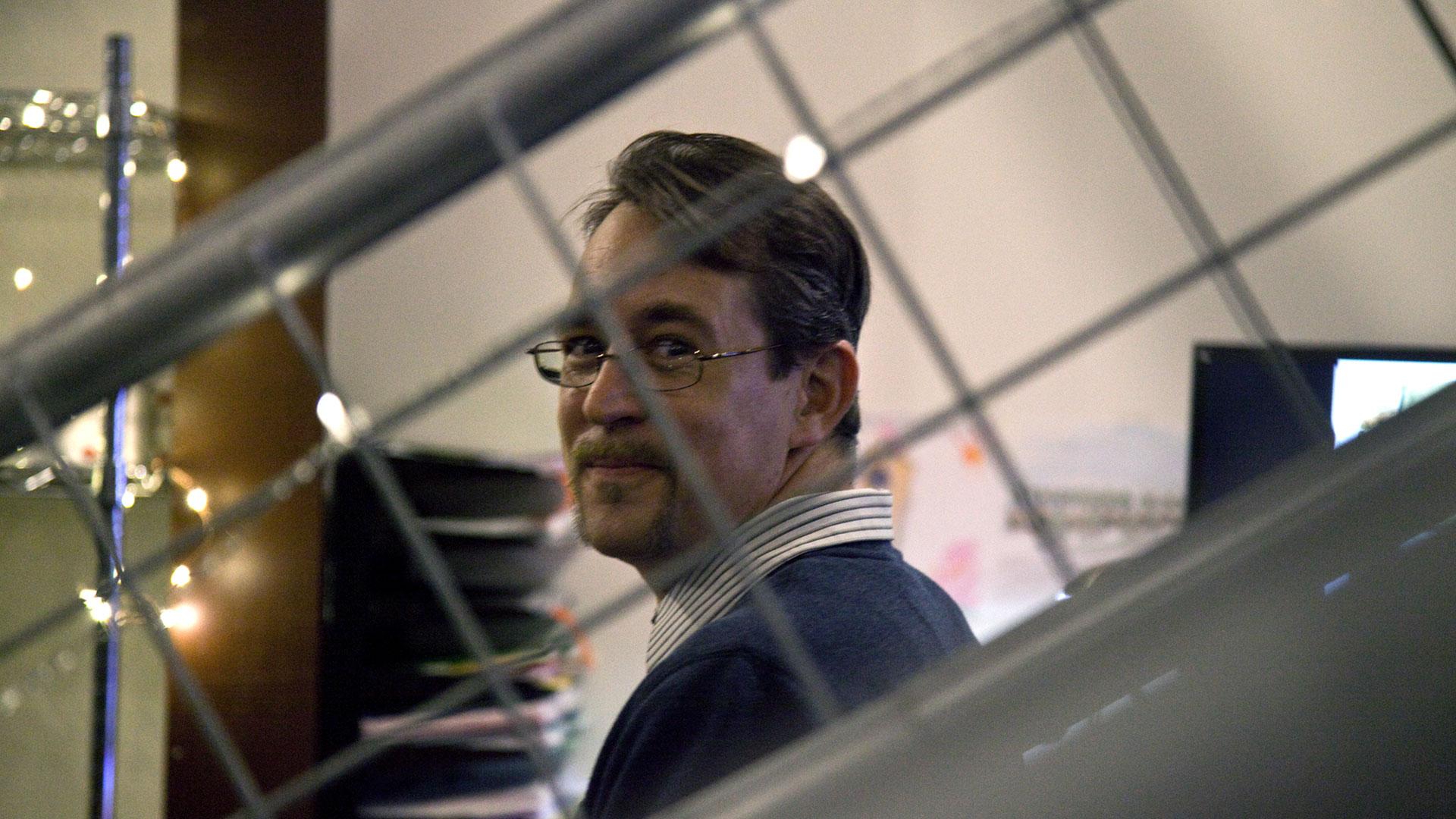 Party attendee smiling at camera through grated staircase railing.