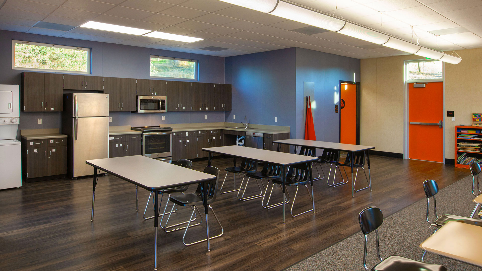Interior of classroom with tables and kitchen area behind.