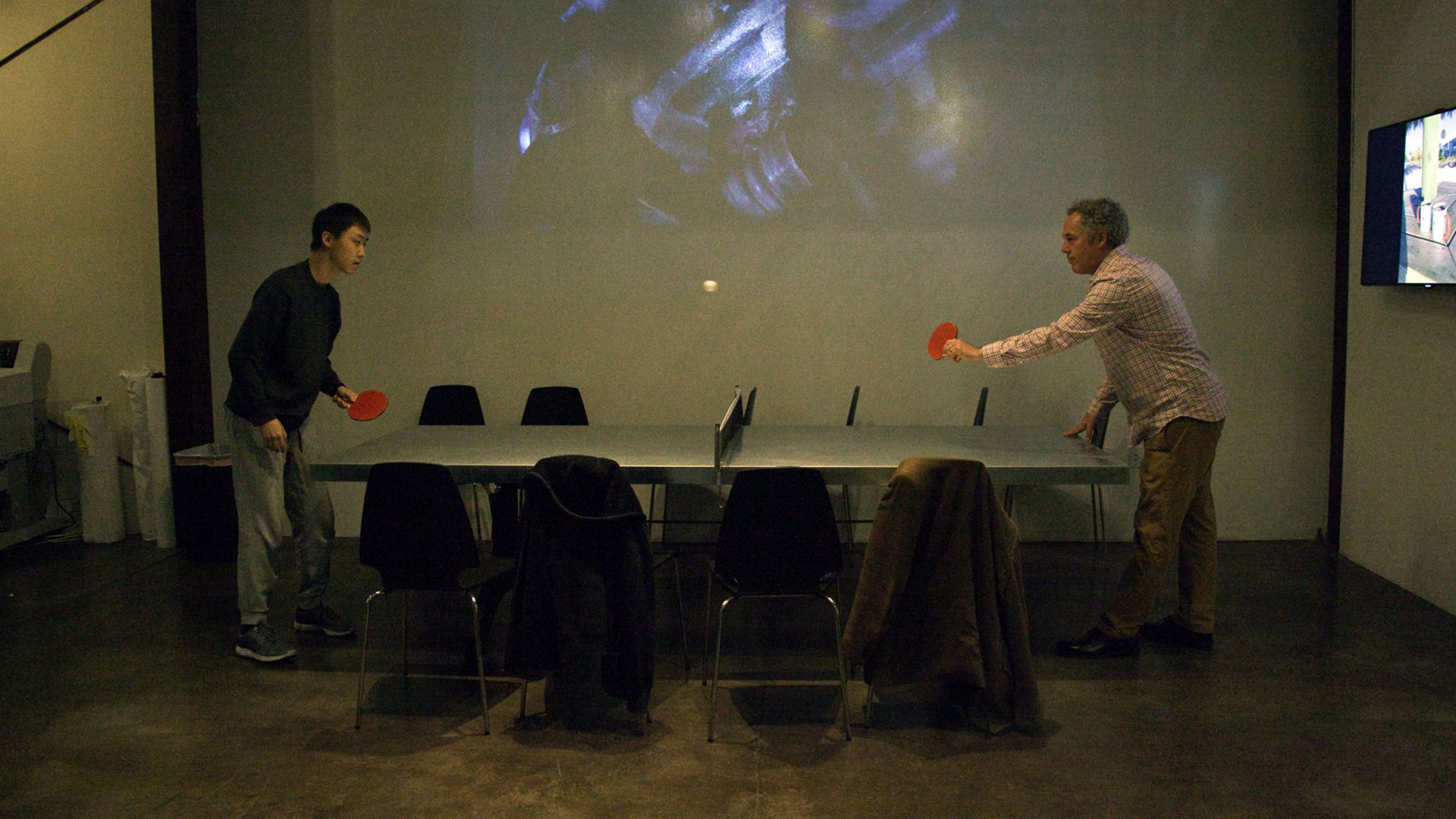 Two people playing ping pong on conference table.