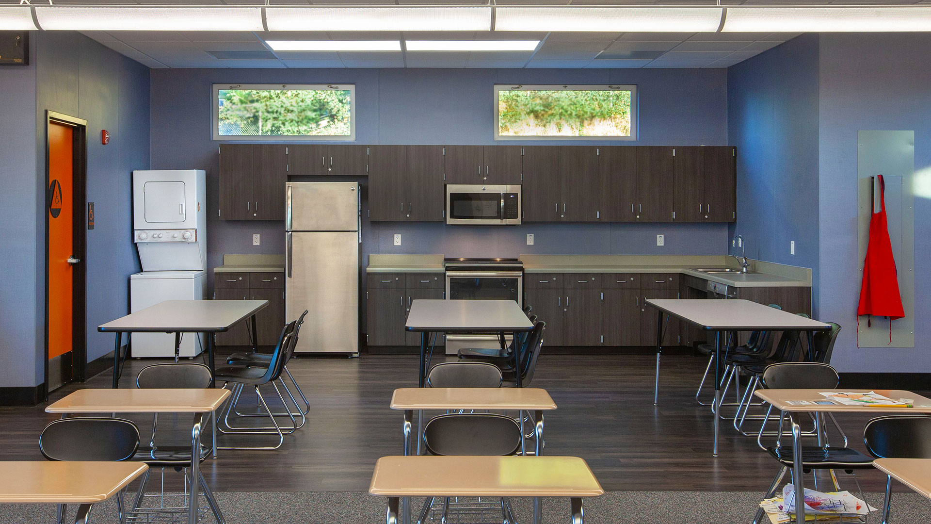 Interior of classroom with tables and kitchen area behind.