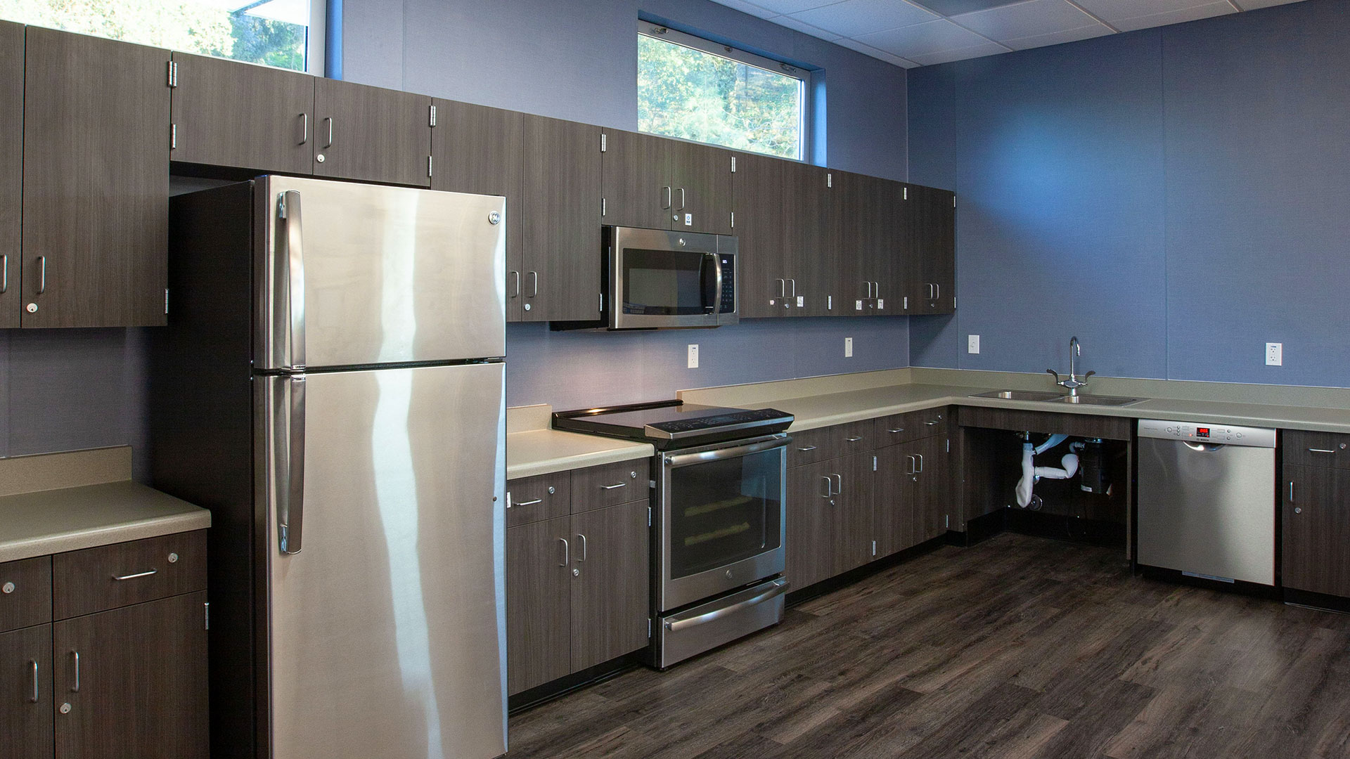 Kitchen area in classroom, with gray cabinets and sleek gray wooden vinyl flooring.