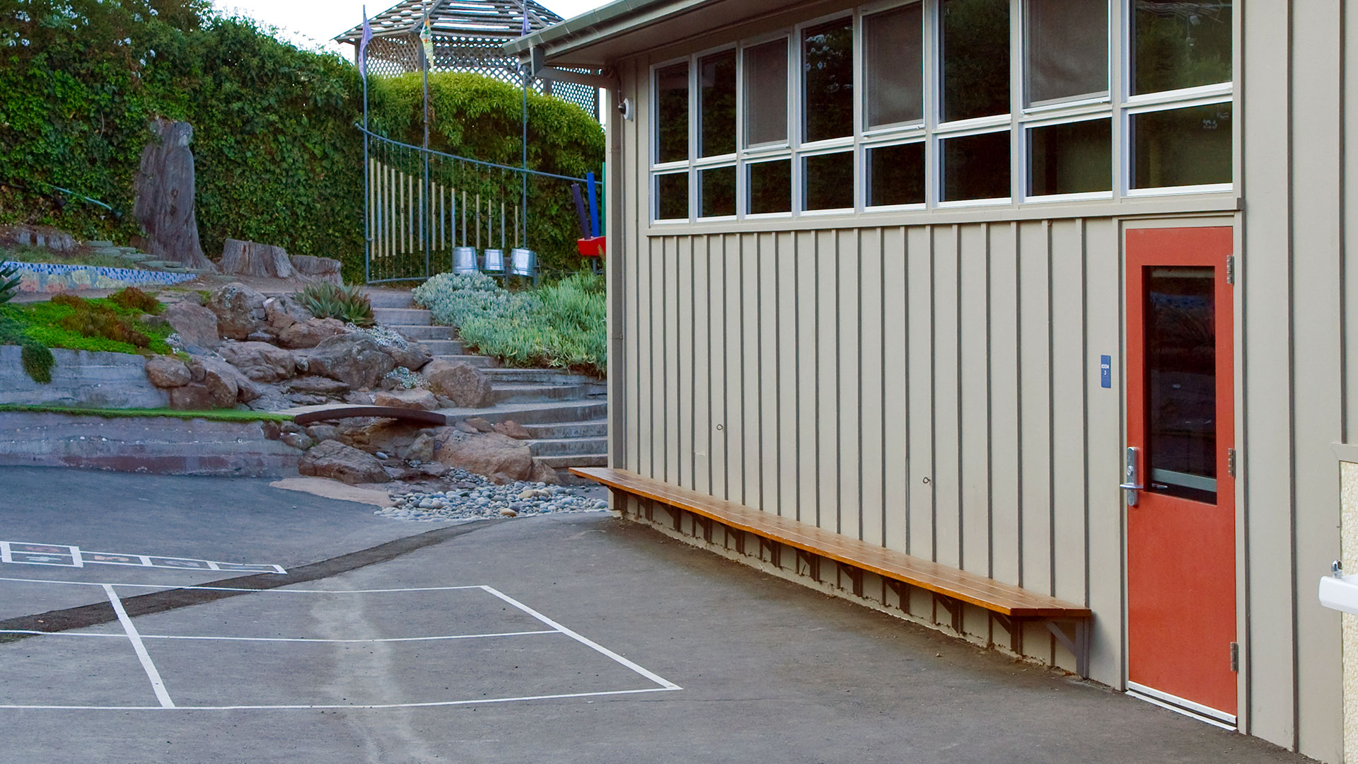 New classroom exterior with paneled walls and high windows, and new green area behind.