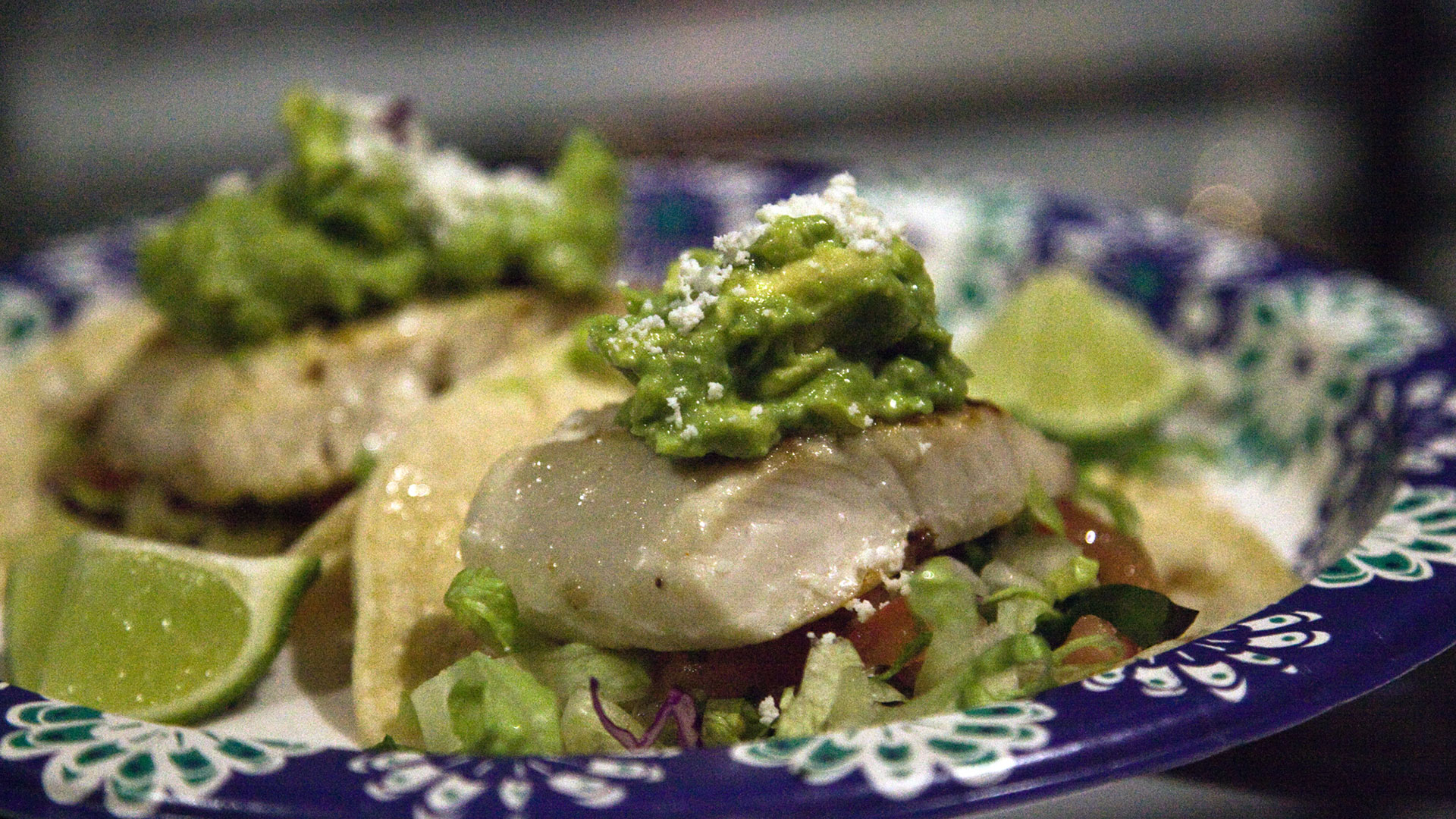 Closeup of food served, tacos with meat served on bed of greens, and a dollop of guacomole on top