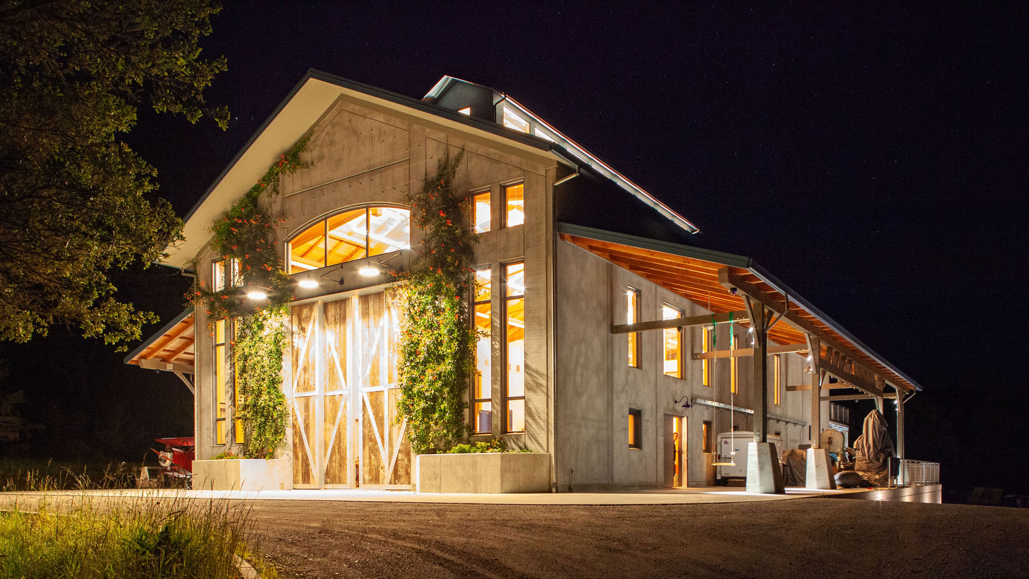 Exterior of barn at night, entrance lit up and windows glowing from inside.