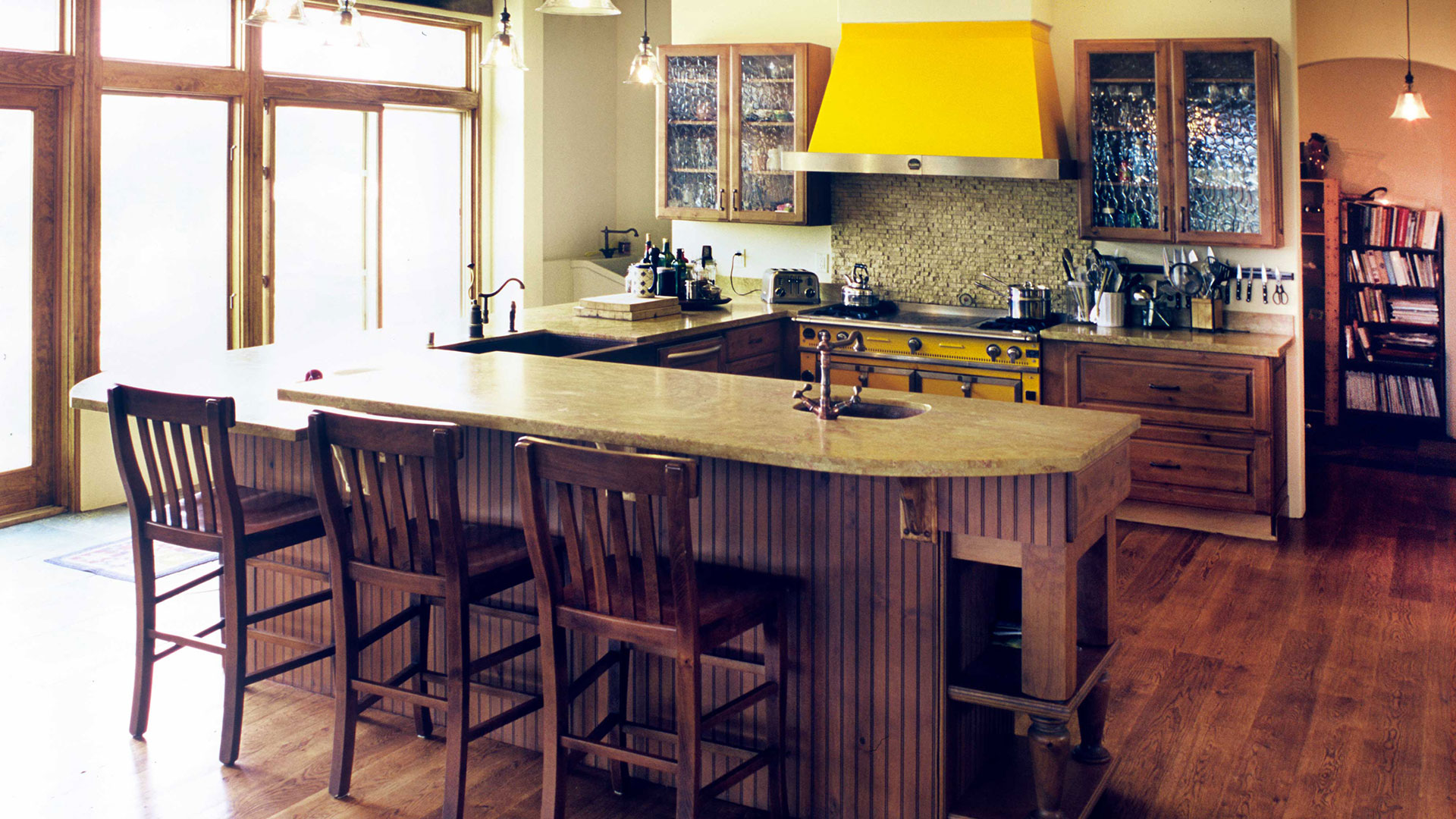 Interior kitchen with rustic Italian aesthetic, 3 wooden chairs, cabinets, and a stone countertop.