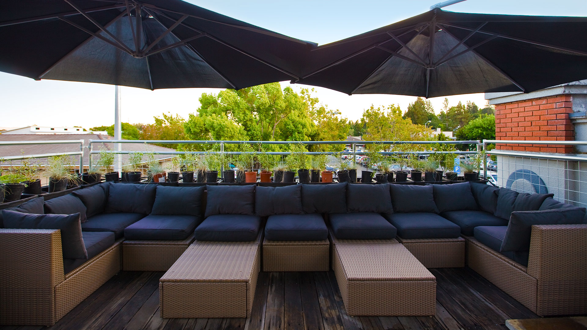 Upper, outdoor mezzanine over office entrance, with outdoor furniture and umbrellas, and surrounded by planters