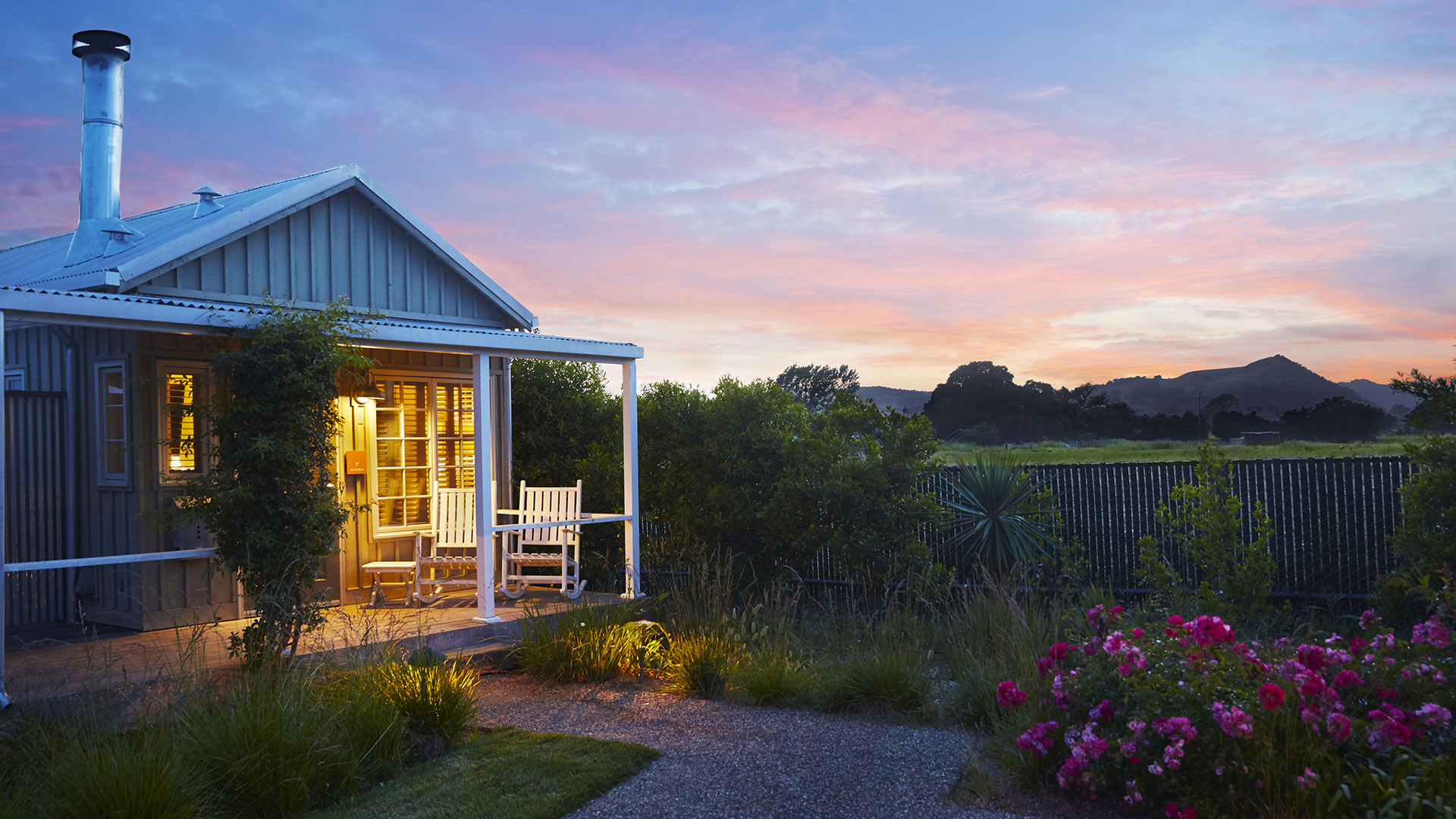 Cottage at dusk, front porch illuminated in soft yellow, and sunset in background.