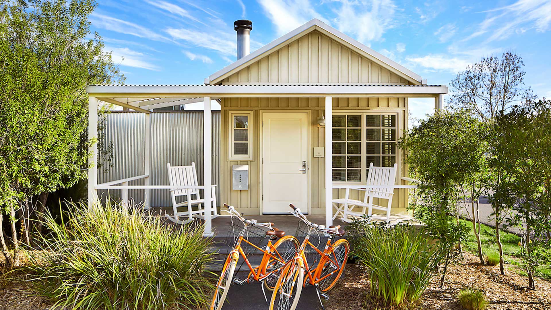 Front of quaint, white cottage, with two bikes and rocking chairs.