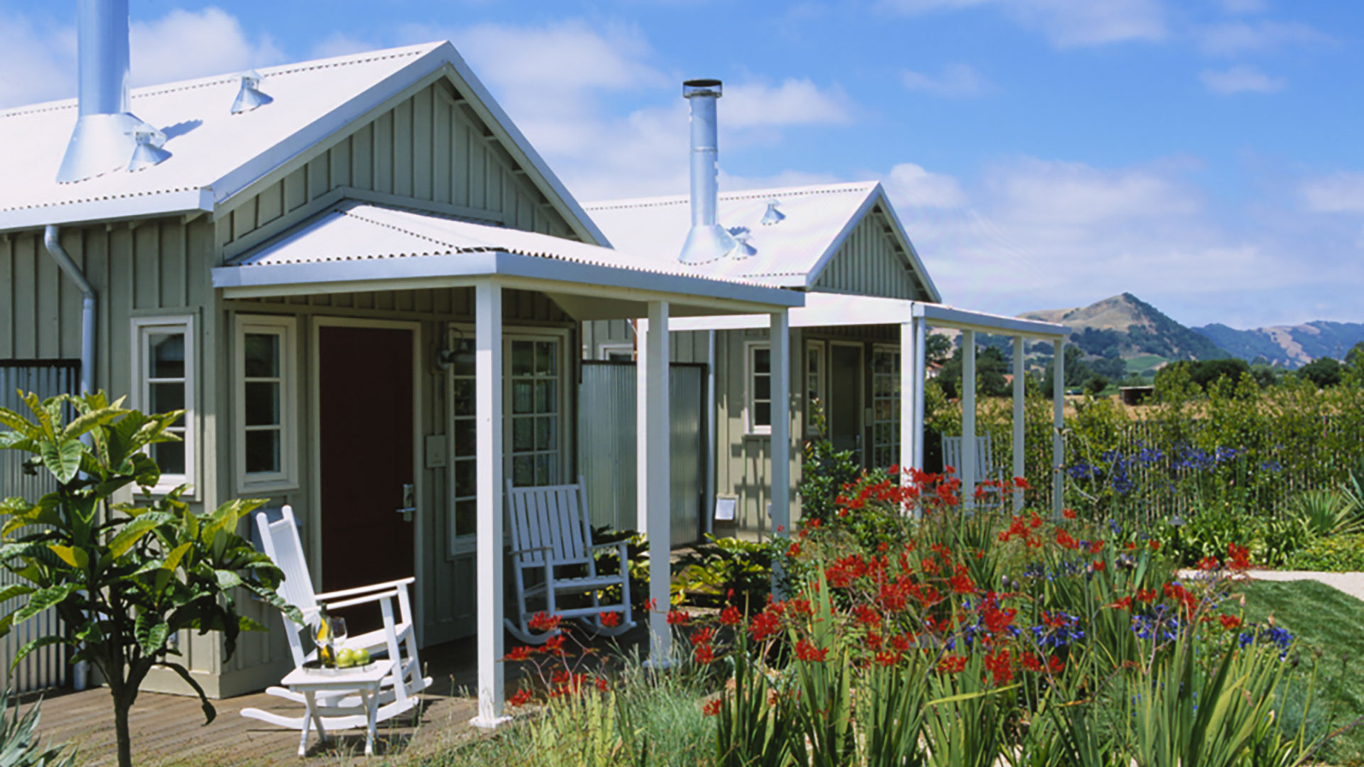 Small white cottages with metal paneling, flowers outside and neighboring cottages.