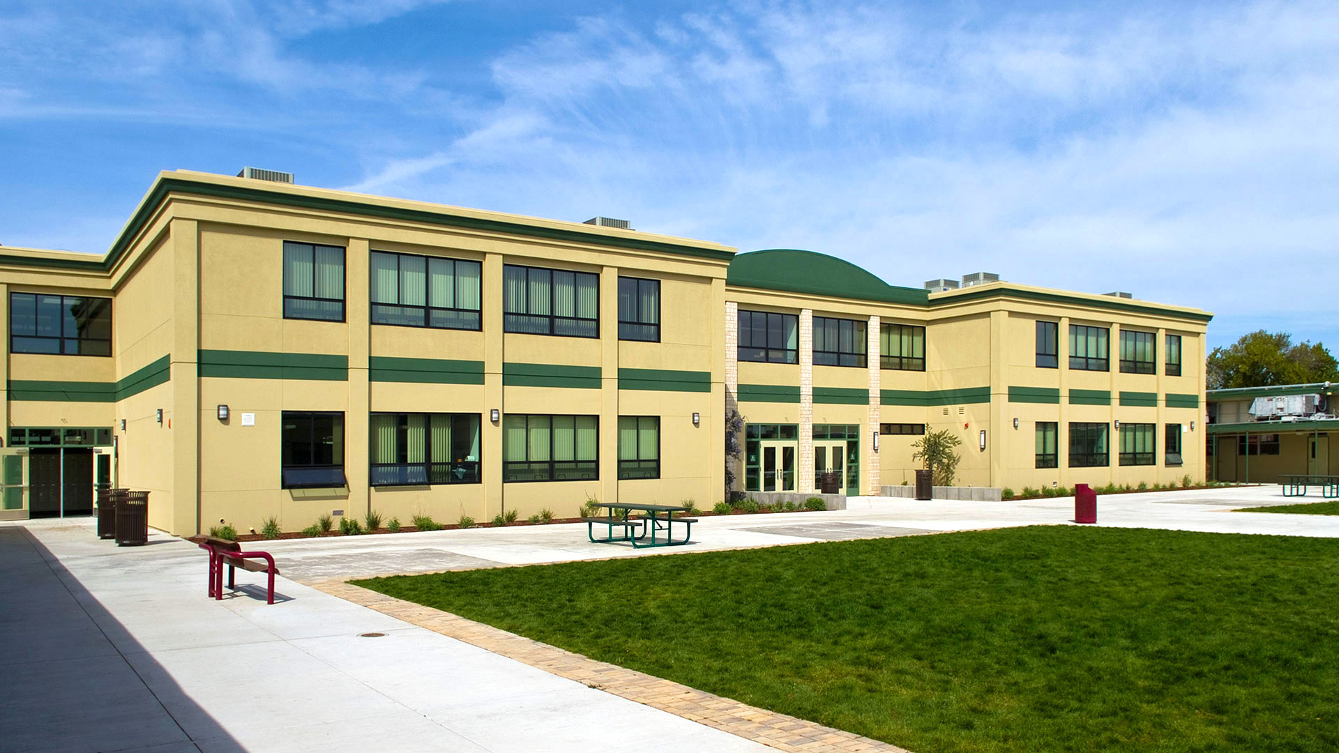 Two story modular classroom wing with beige walls and green details, and grass field in front.