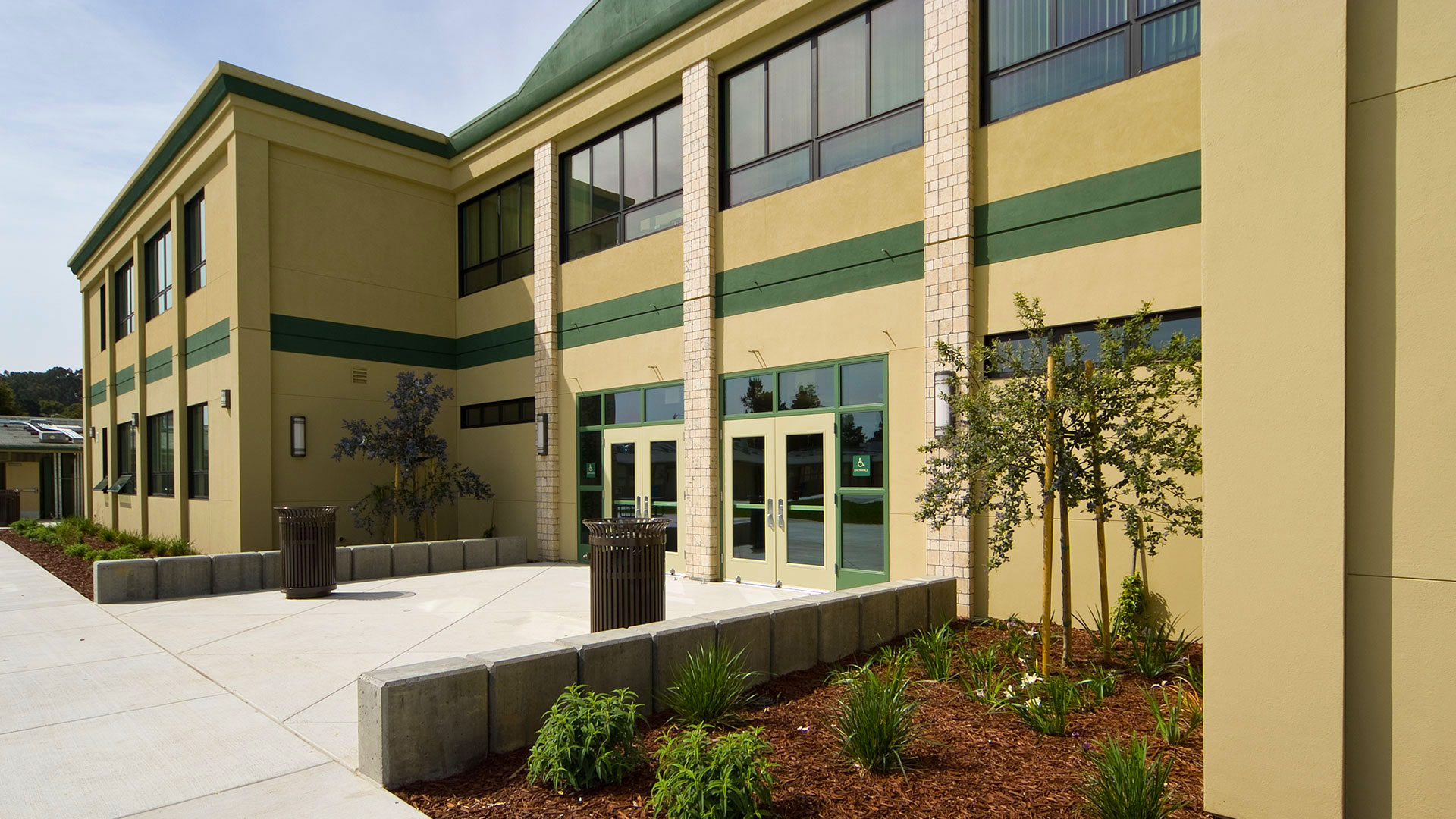 Two story modular classroom wing with beige walls and green details, and green area flanking entrance..