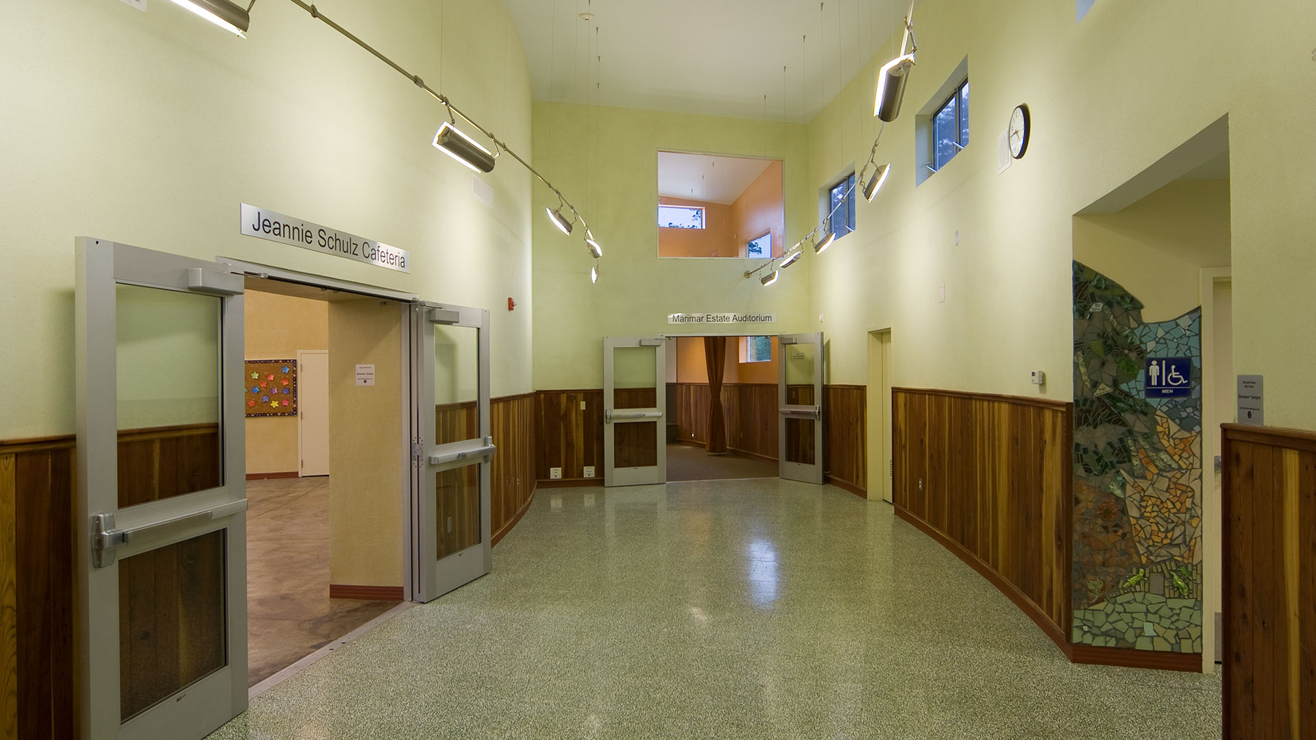 Hallway interior, double height ceilings above yellow walls with wooden panel wainscot.