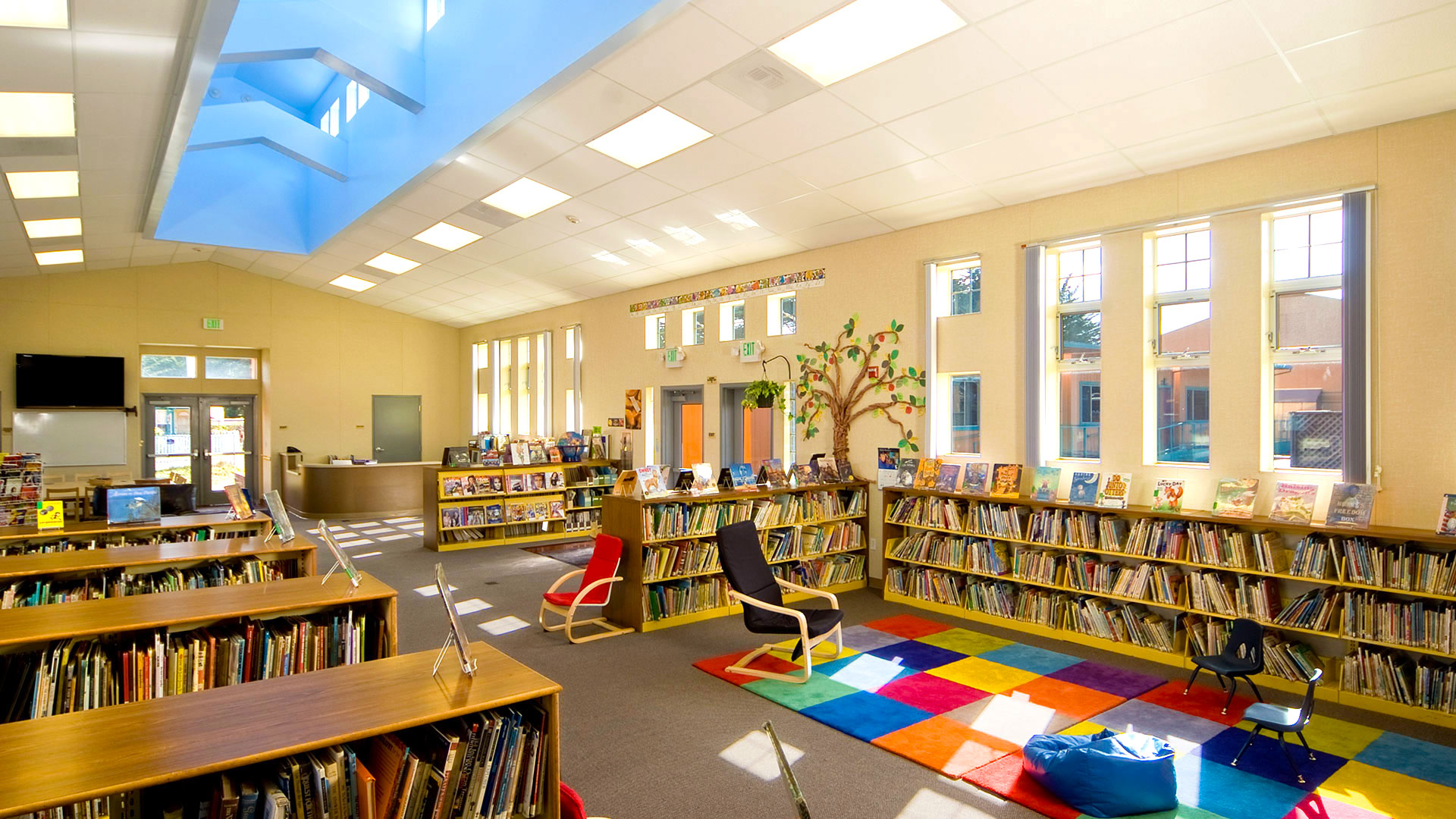 Interior of library, bookshelves and seating organized around with bright fun rugs group reading.