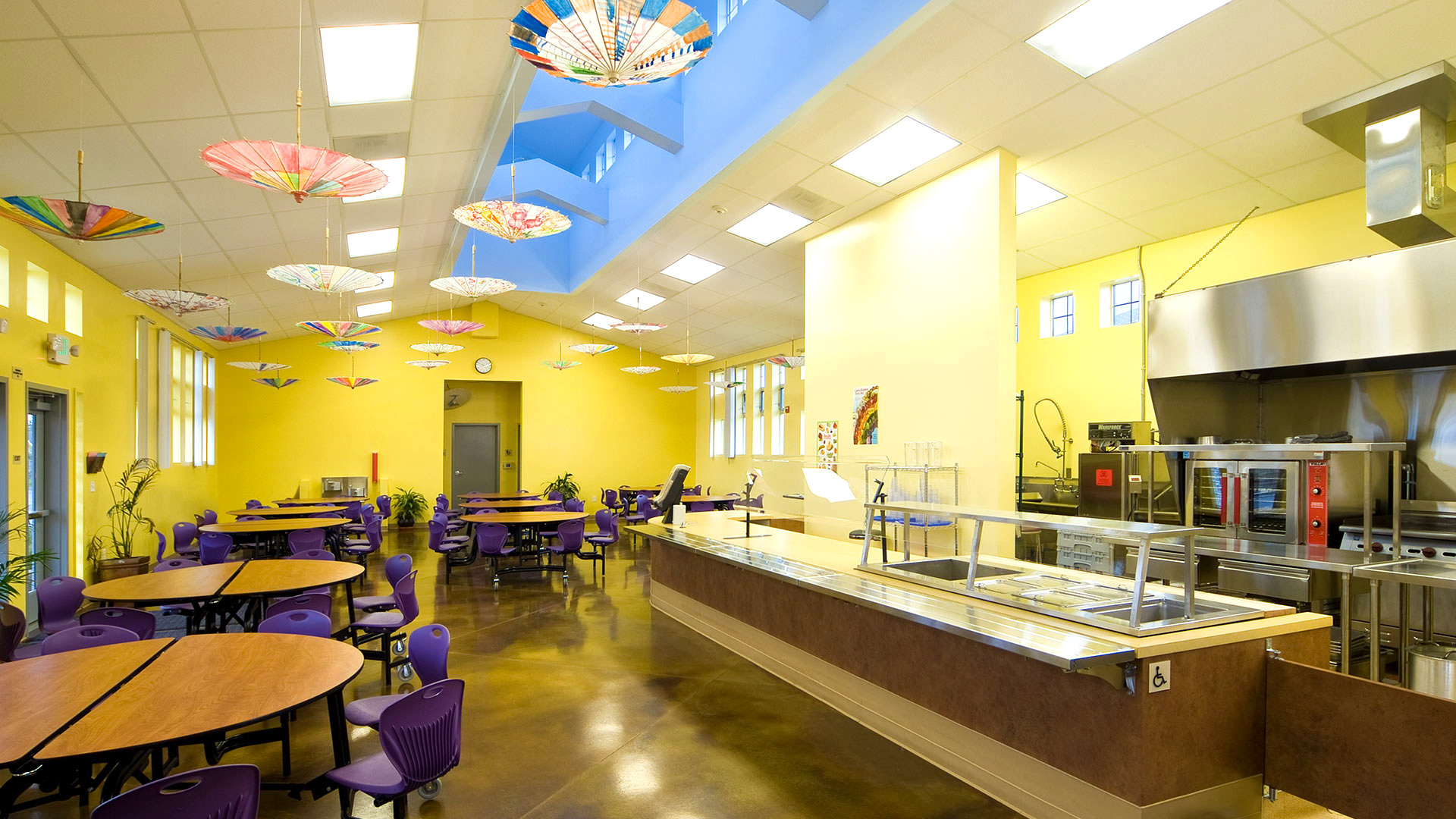 Interior of cafeteria, highlighting on serving area. Fun umbrellas hang from the ceiling for artsy effect.
