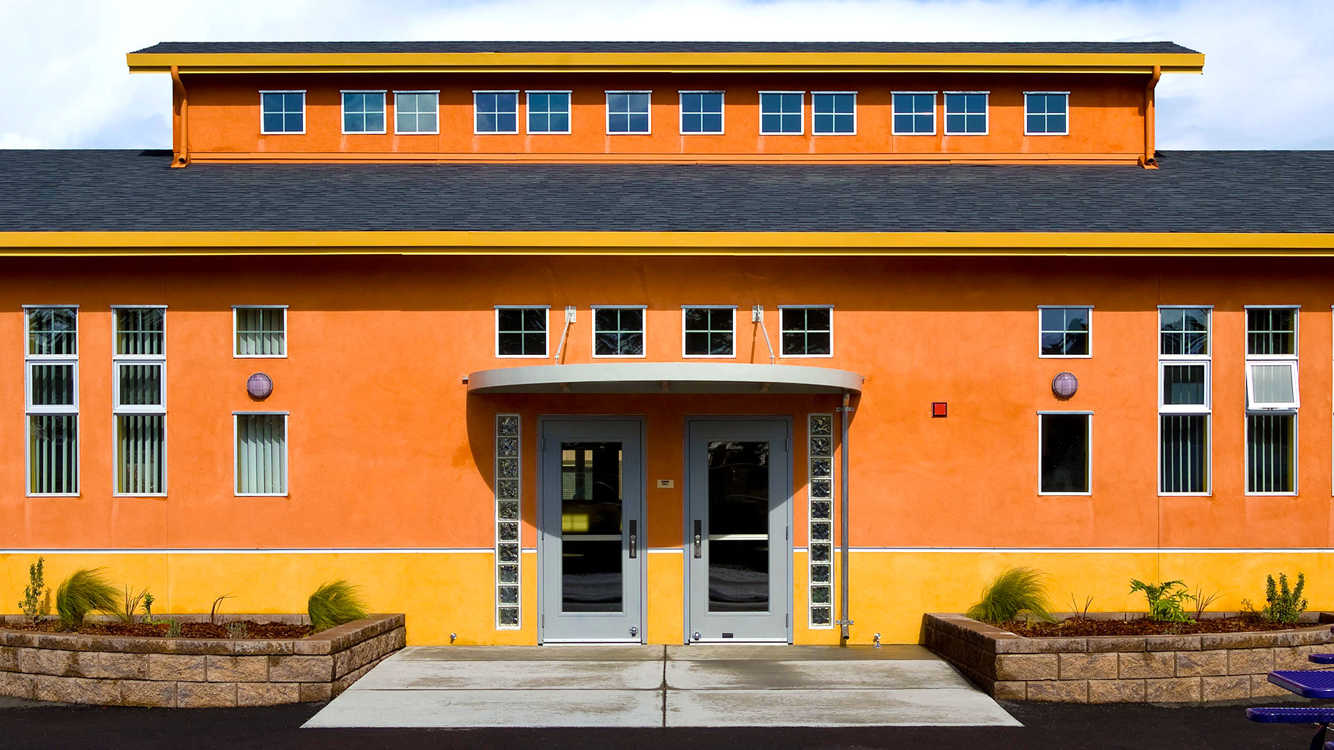 Exterior of completed cafeteria, focusing on main side entrance, flanked with windows on either side and an awning above.