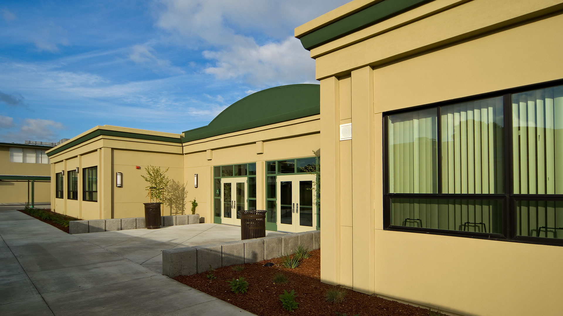 One story modular classroom wing with beige walls and green details, and green area flanking entrance..