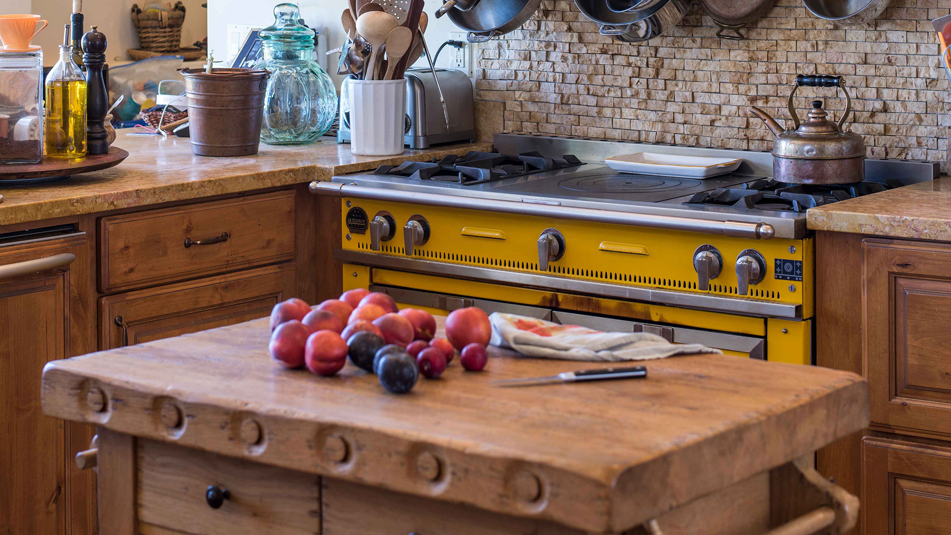 Closeup of kitchen island, a rustic wooden block, with fruit on top. Yellow stove behind.