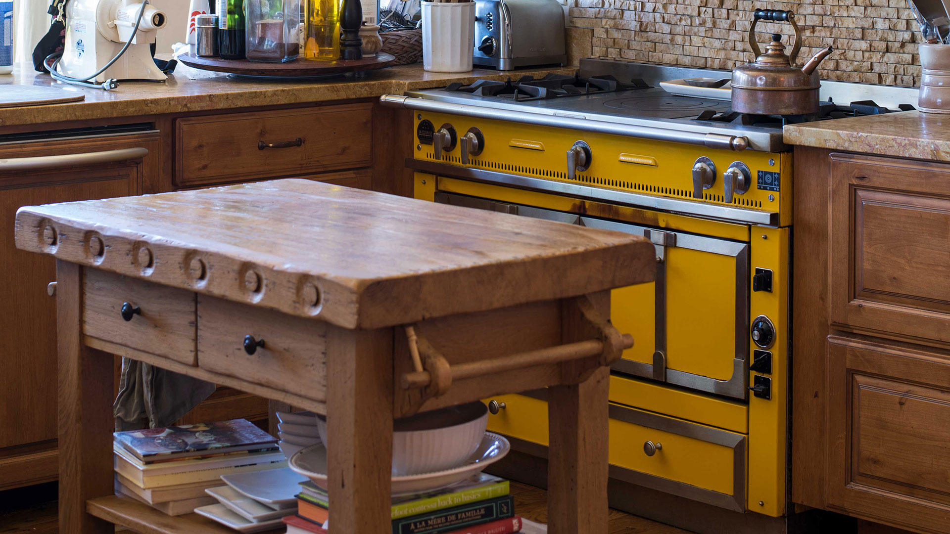 Closeup of wooden kitchen island piece and antique italian yellow stove behind.