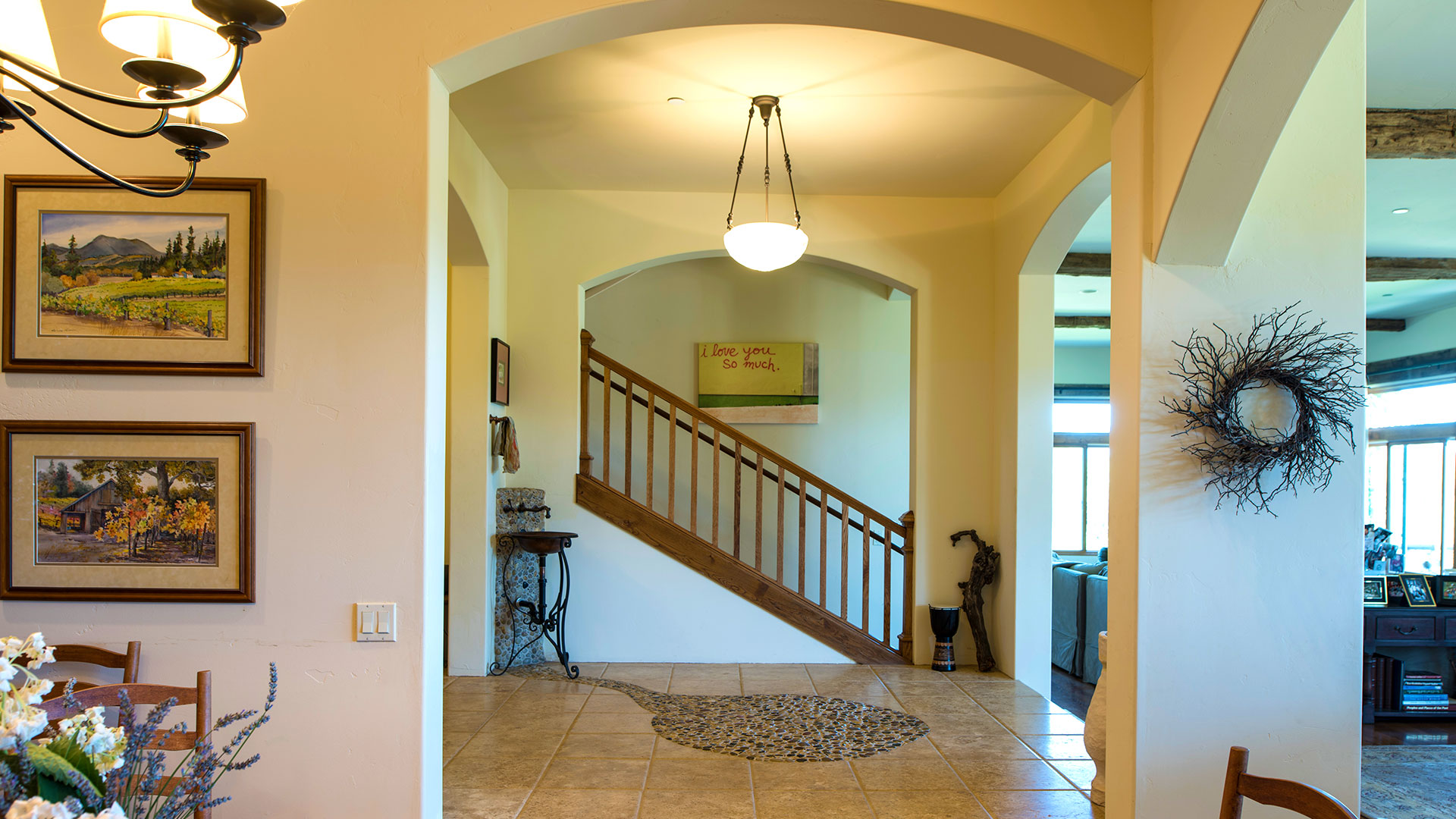 Wide shot of foyer with staircase in background. Inset stone circle leading to sink with hanging light above.