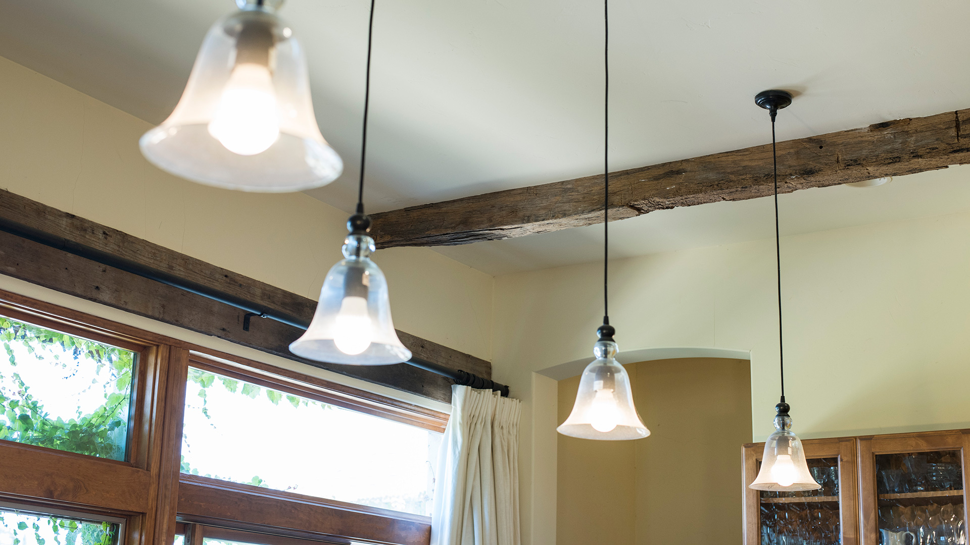 Looking up at hanging lights above kitchen, with exposed wooden ceiling beams behind.