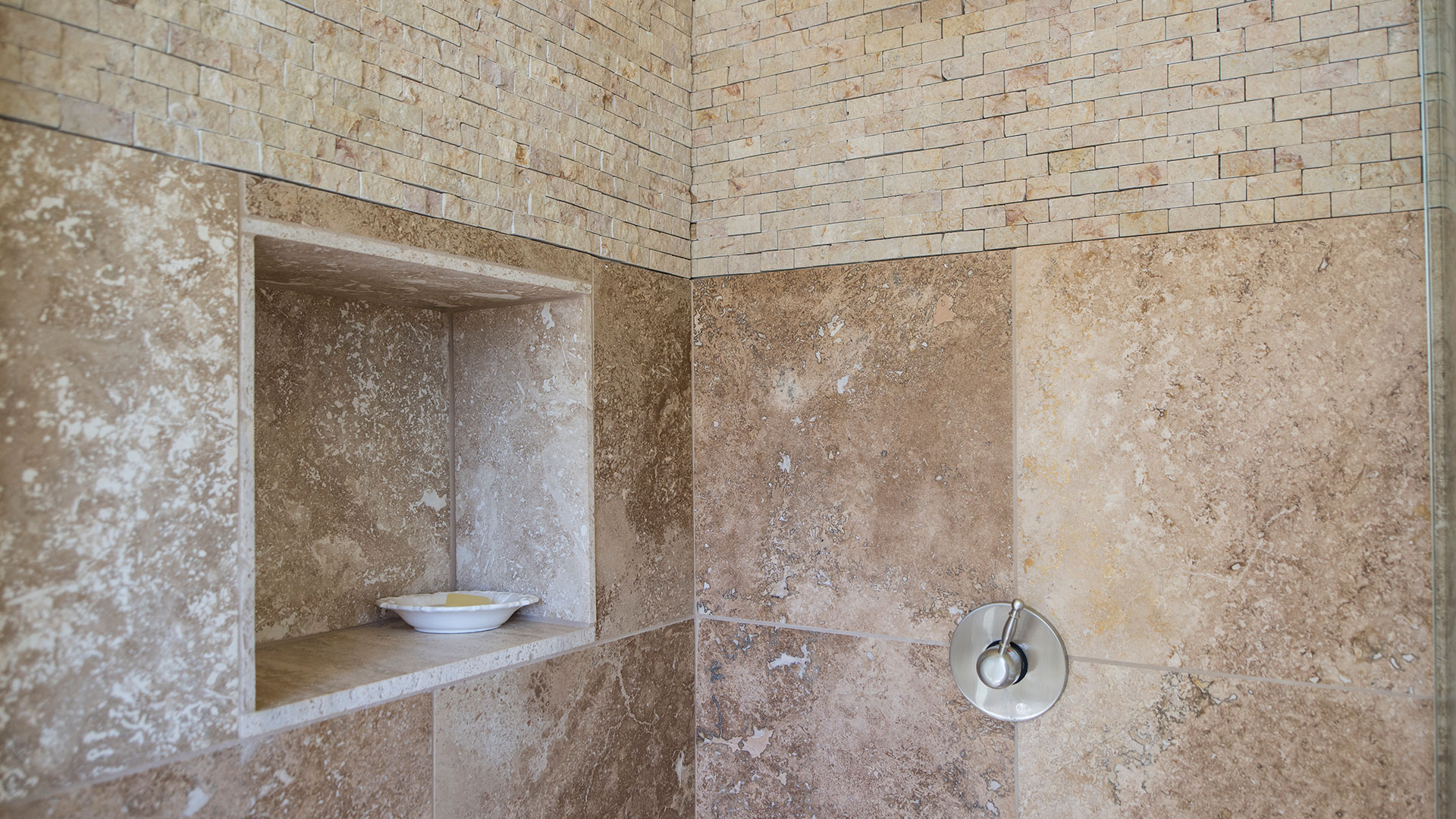 Interior shower with rustic stone tiles, metal valve, and a stone niche.