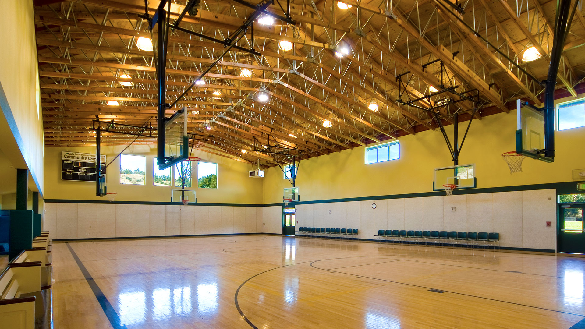 Gymnasium interior and basketball court, with intricate exposed wood trusses above yellow walls and white wainscot.