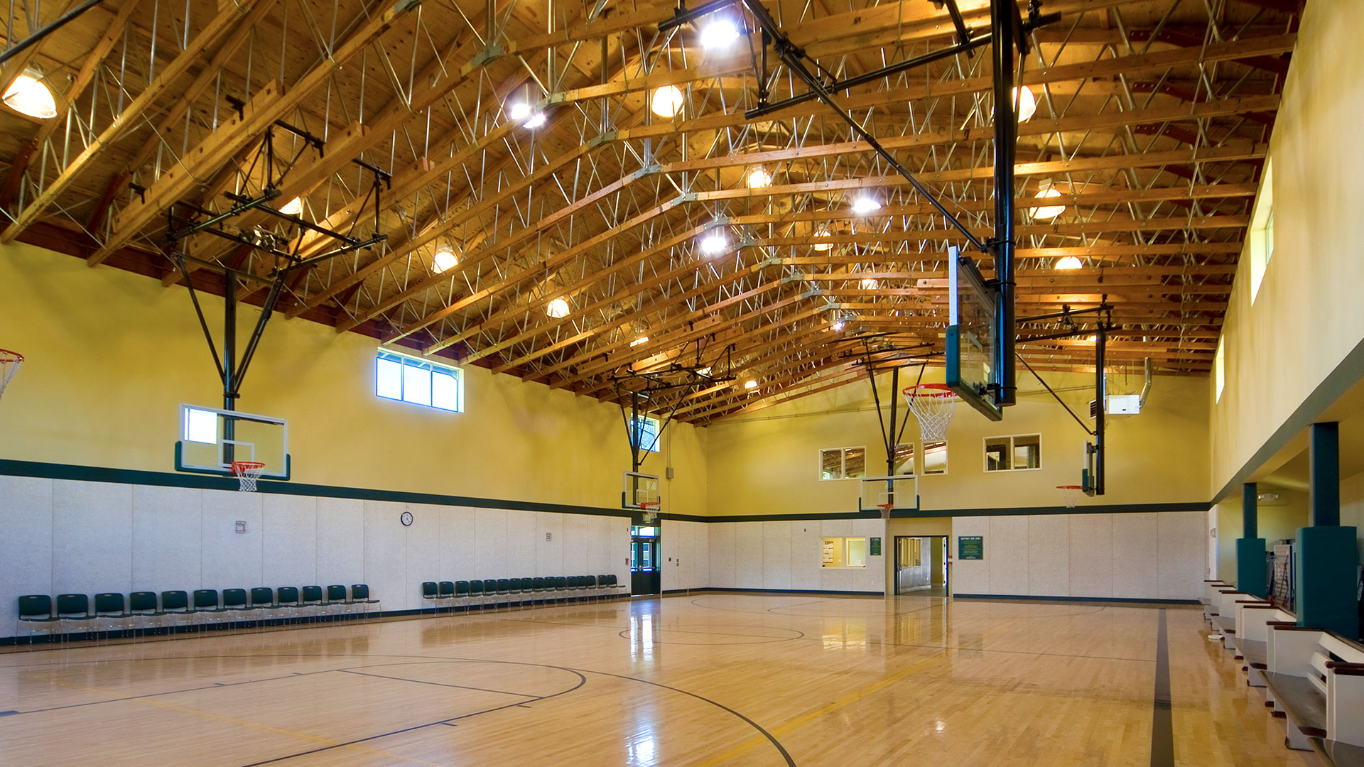 Gymnasium interior and basketball court, with intricate exposed wood trusses above yellow walls and white wainscot.