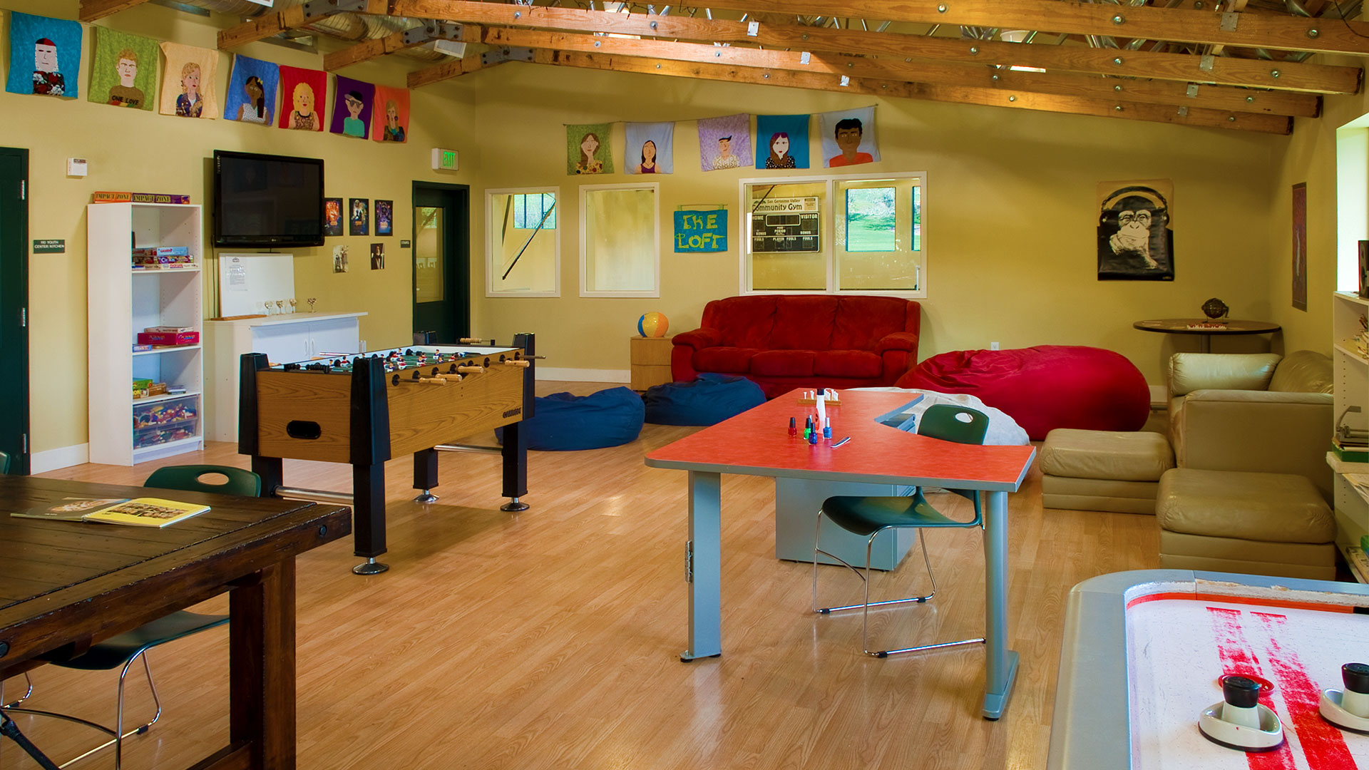 Classroom and student area, with yellow walls covered in artwork and posters, with desks, couches, and foosball.
