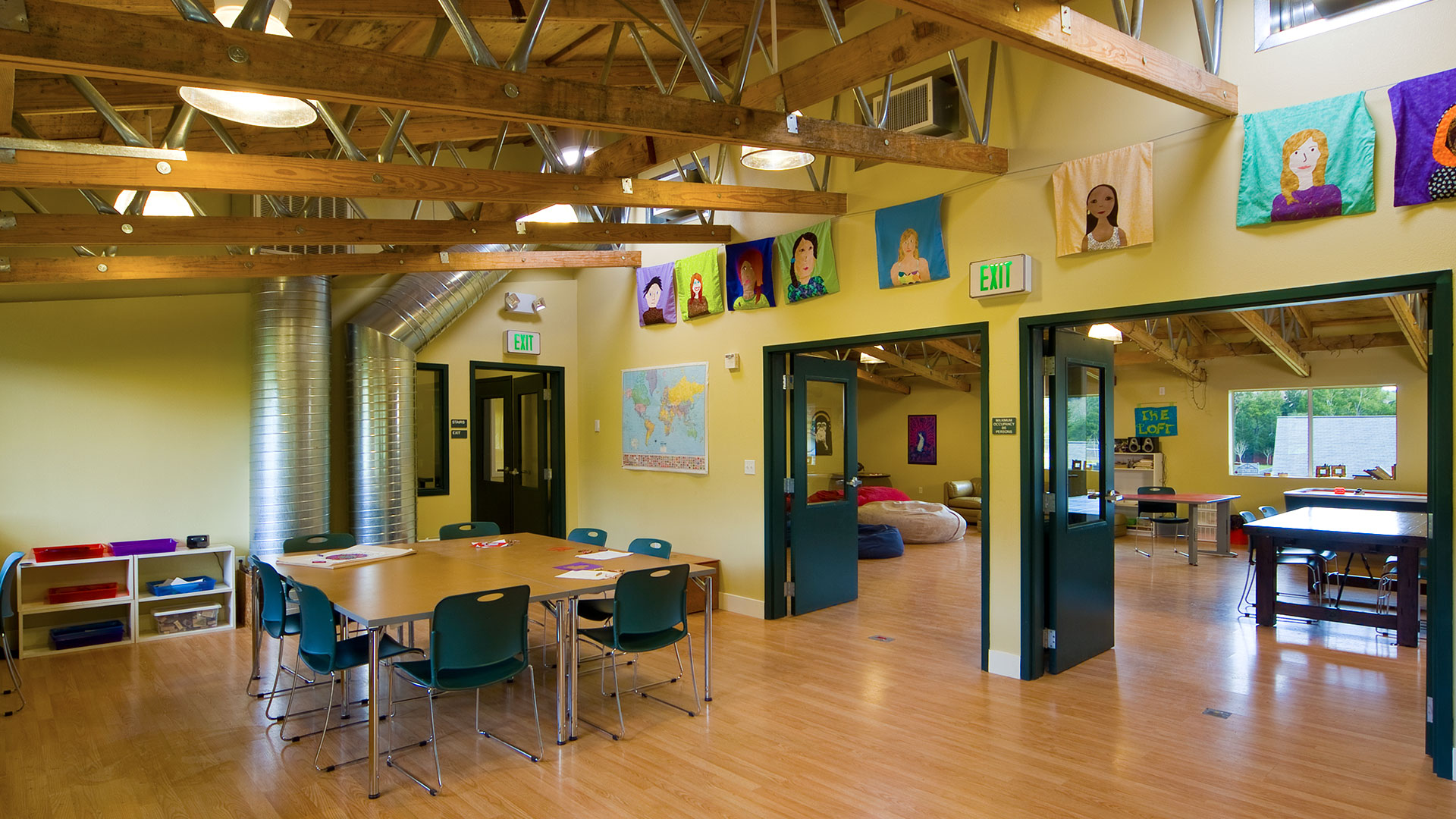 Classroom and student area, with yellow walls covered in artwork and posters, with desks, couches, and foosball.