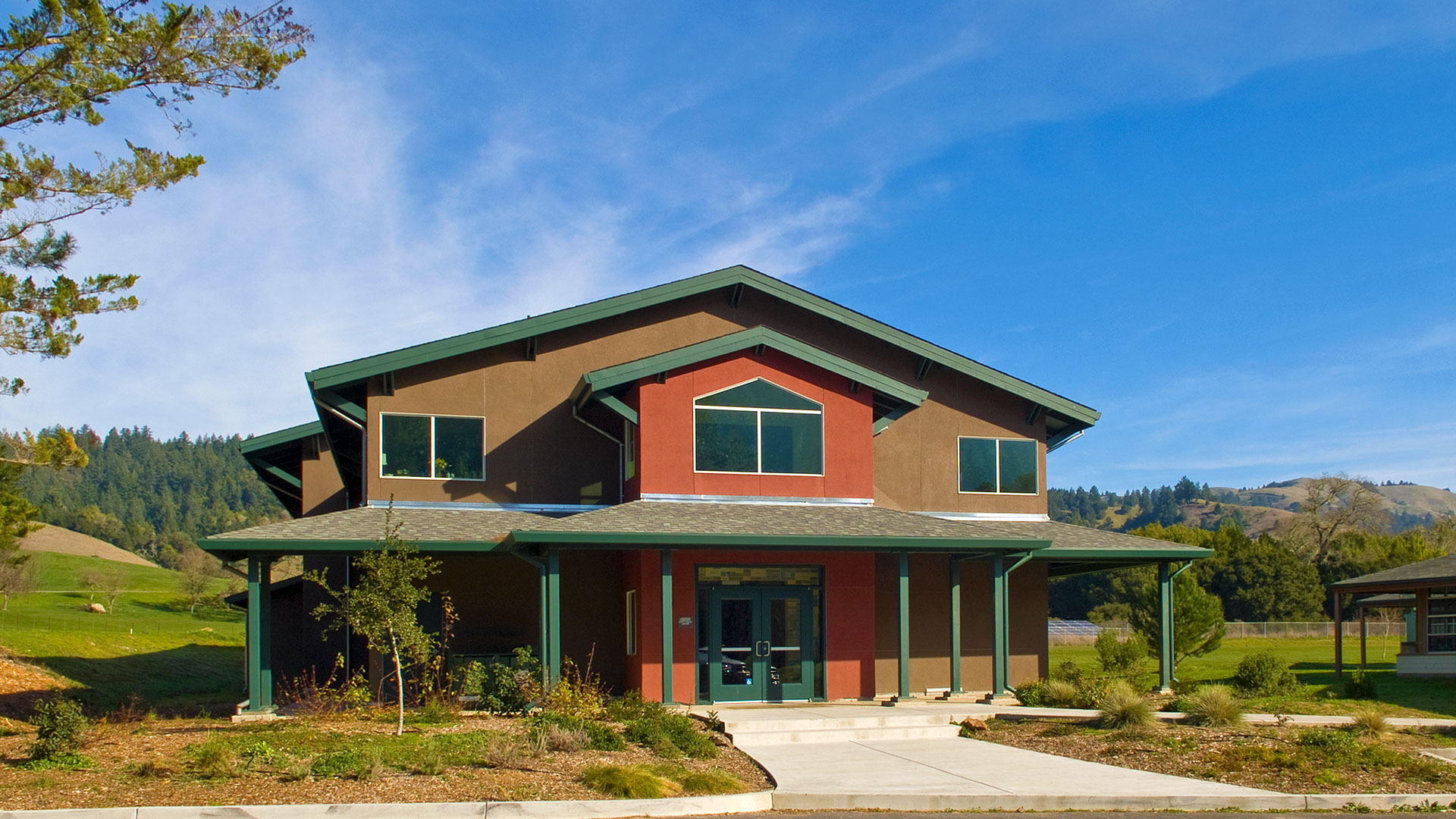 Lagunitas gym with forest and hills in background. Brown two story walls with sectioned red two story entrance.