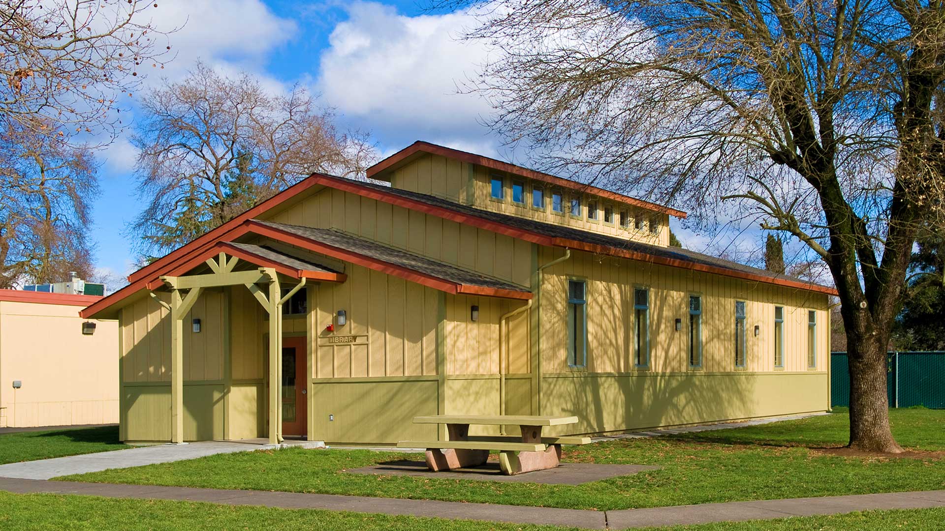 Library building built next to tree, wih yellow paneling walls and gray roofs with orange trim