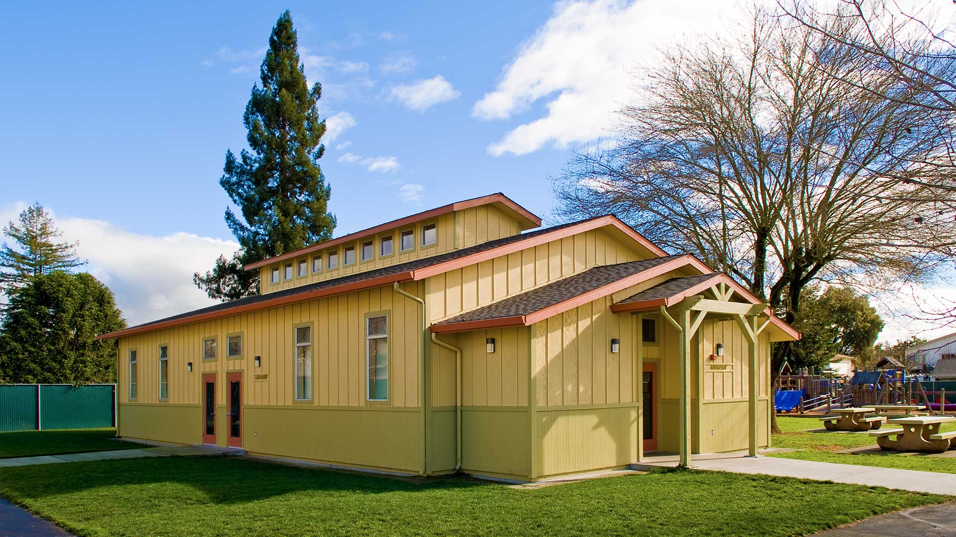 Library building entrance with yellow walls and light green wainscot, with playground behind.